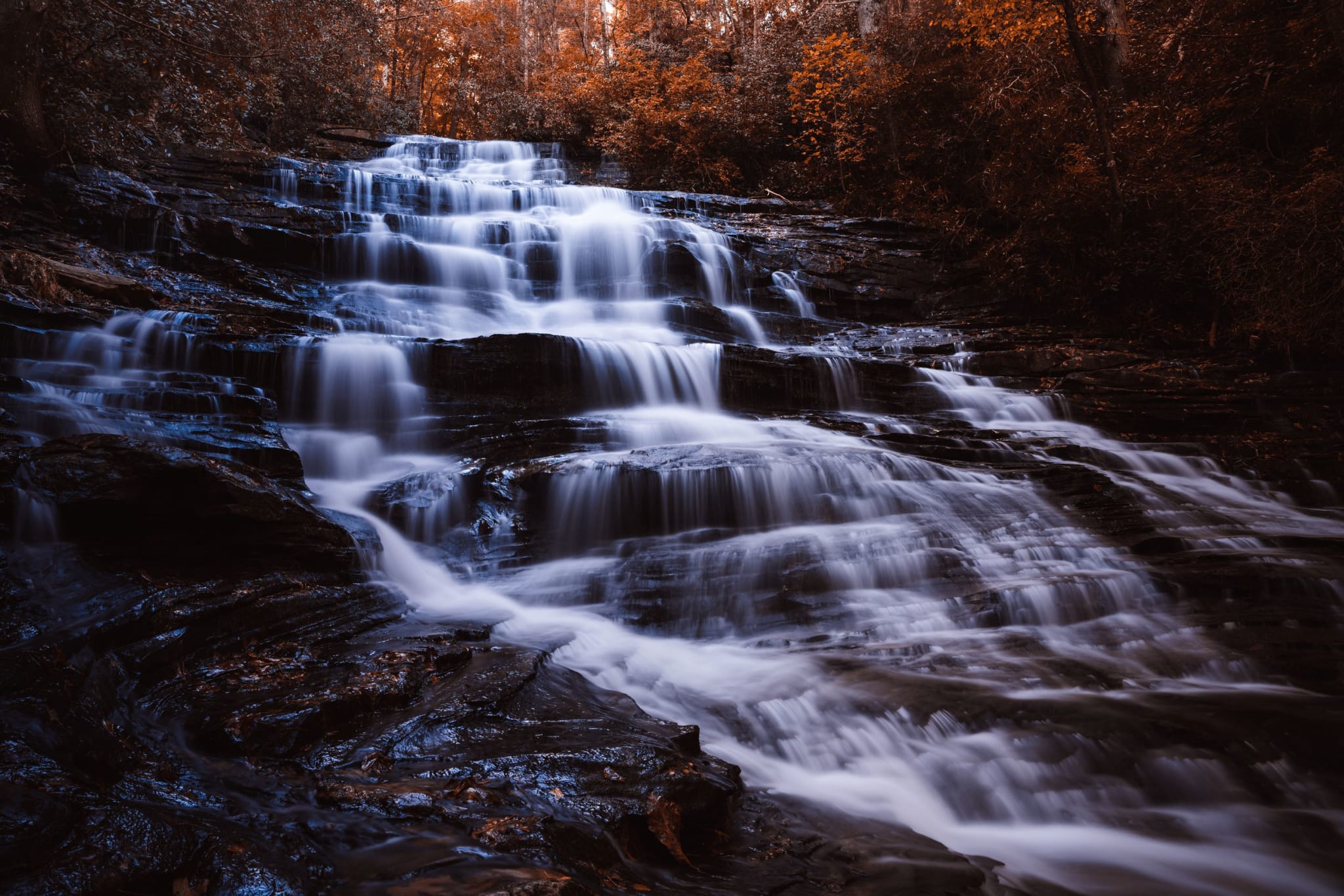 A cascading waterfall flows over multiple rock tiers, surrounded by autumn foliage in Atlanta, Georgia.