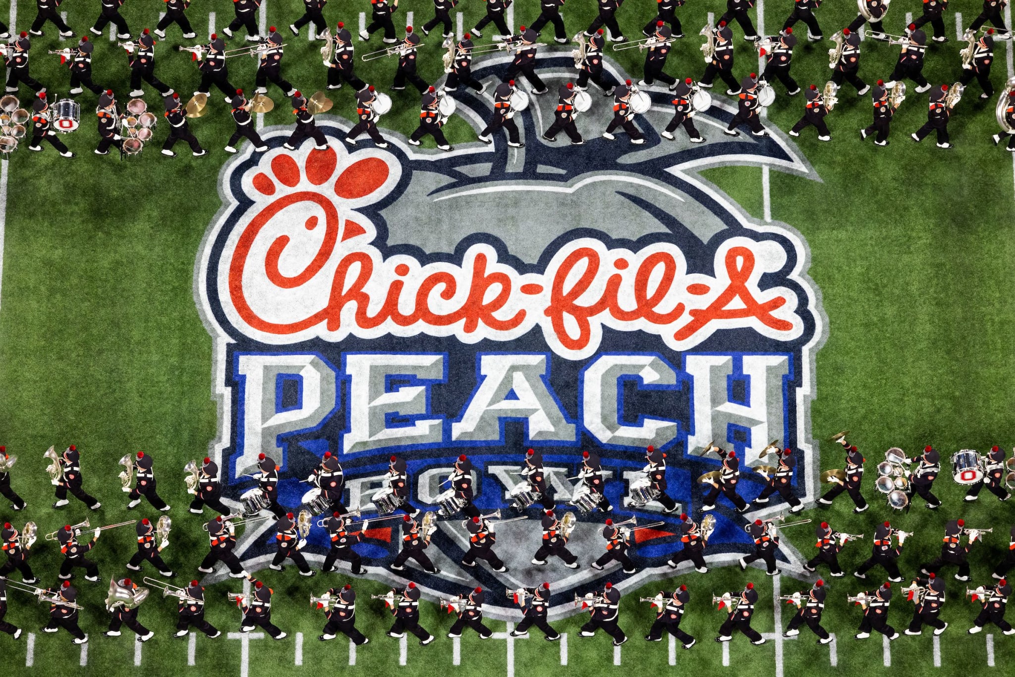 A marching band performs on a football field with a Chick-fil-A Peach Bowl logo at center in Atlanta, Georgia.
