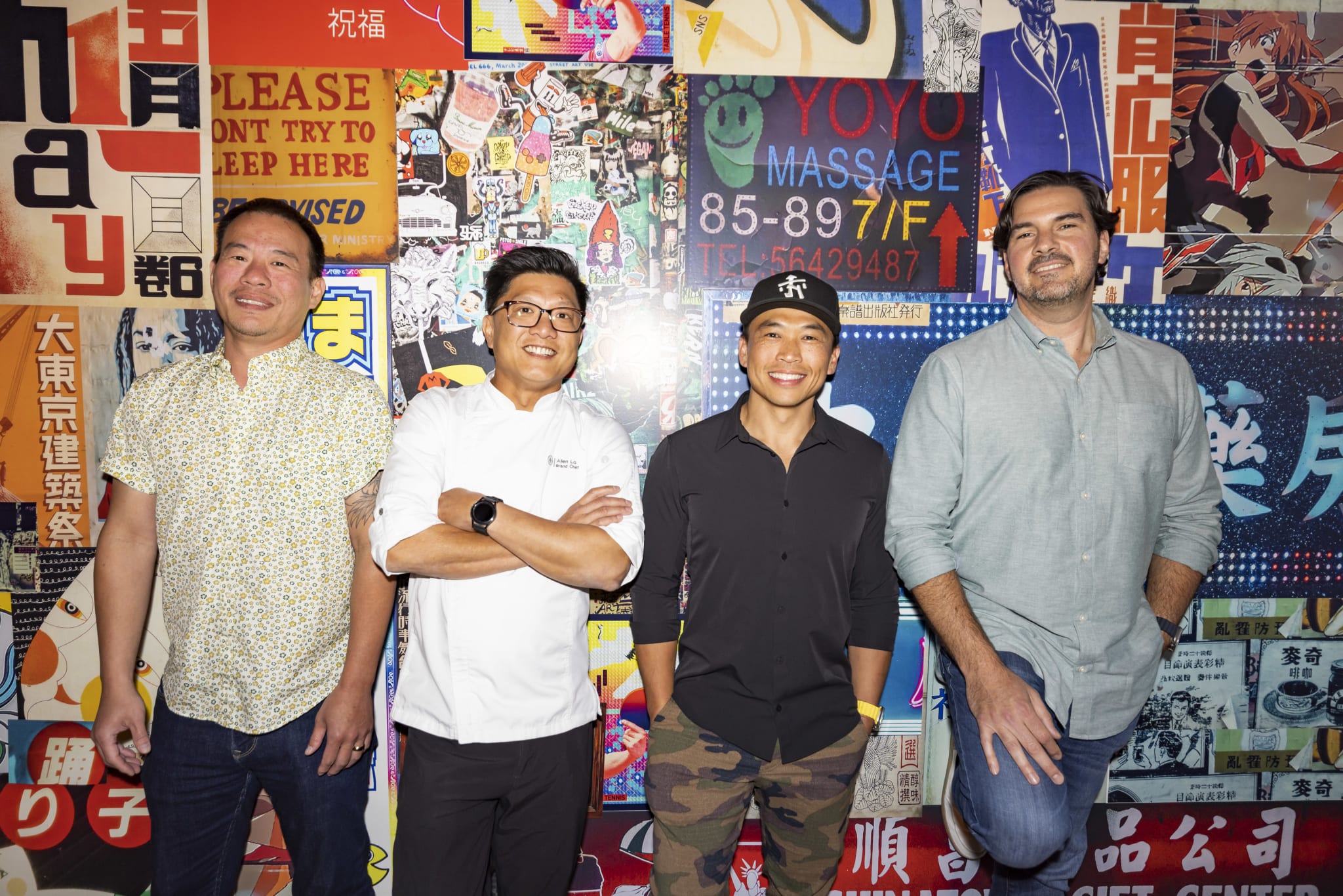Four smiling Asian men stand in front of a colorful wall covered in Japanese posters and advertisements in Atlanta, Georgia.