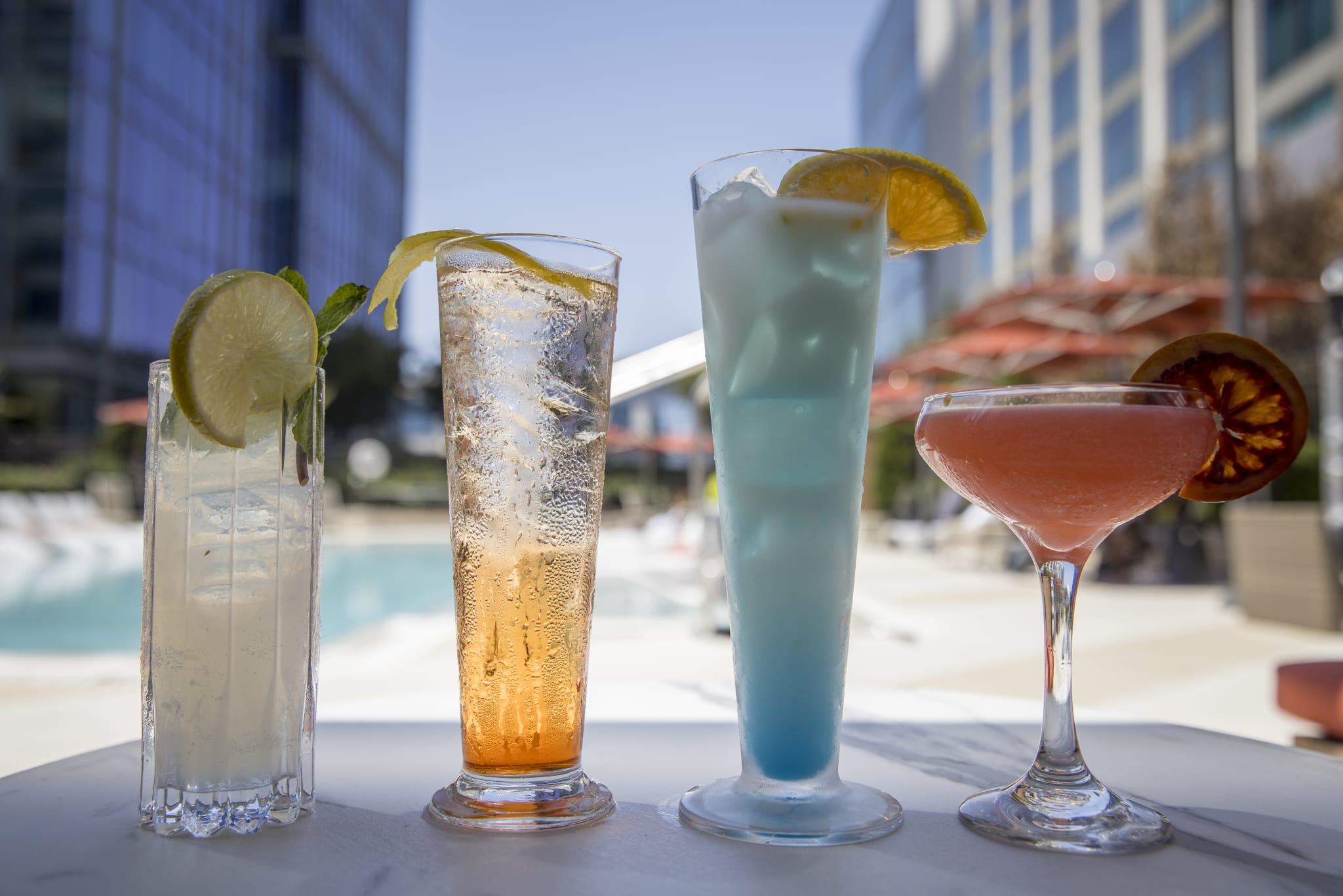 Best Places to Drink and Eat Outside this Fall in Atlanta 2 Four colorful cocktails with citrus garnishes are arranged on a table by a poolside in Atlanta, Georgia.