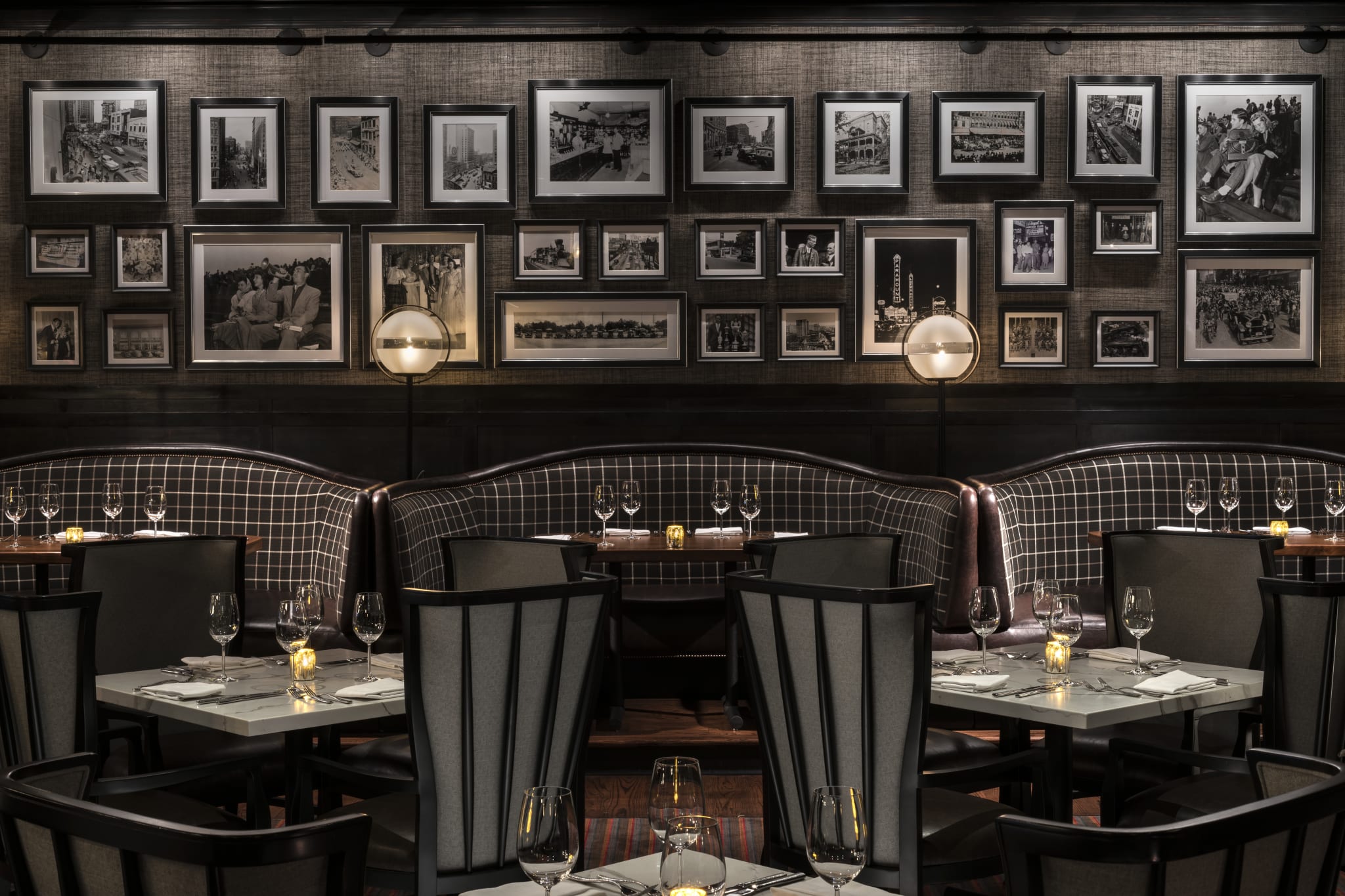 A dimly lit restaurant with a wall of black and white photos and a cozy booth with wine glasses in Atlanta, Georgia.