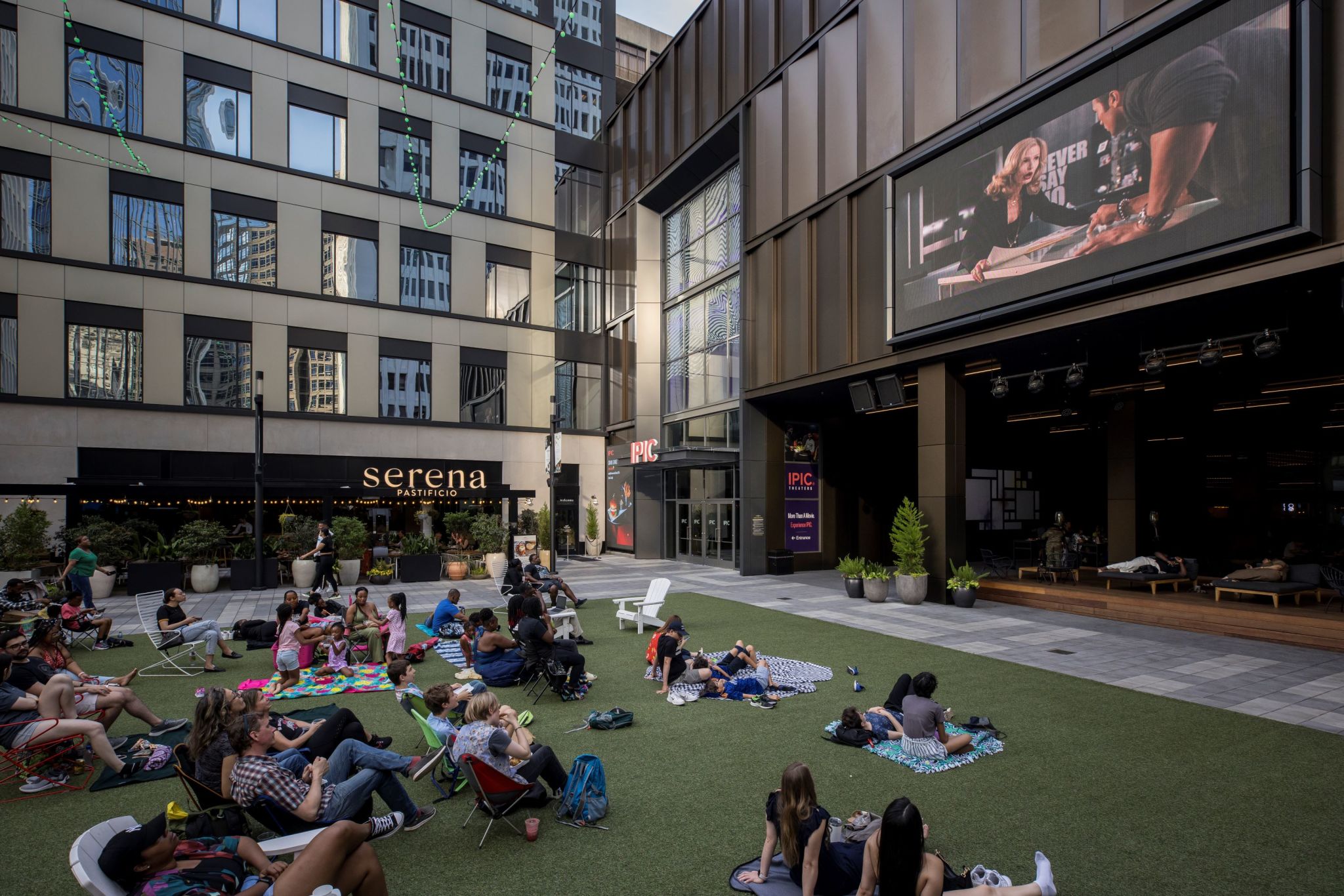 People relax on a grassy rooftop patio with a large screen showing a movie in Atlanta, Georgia.
