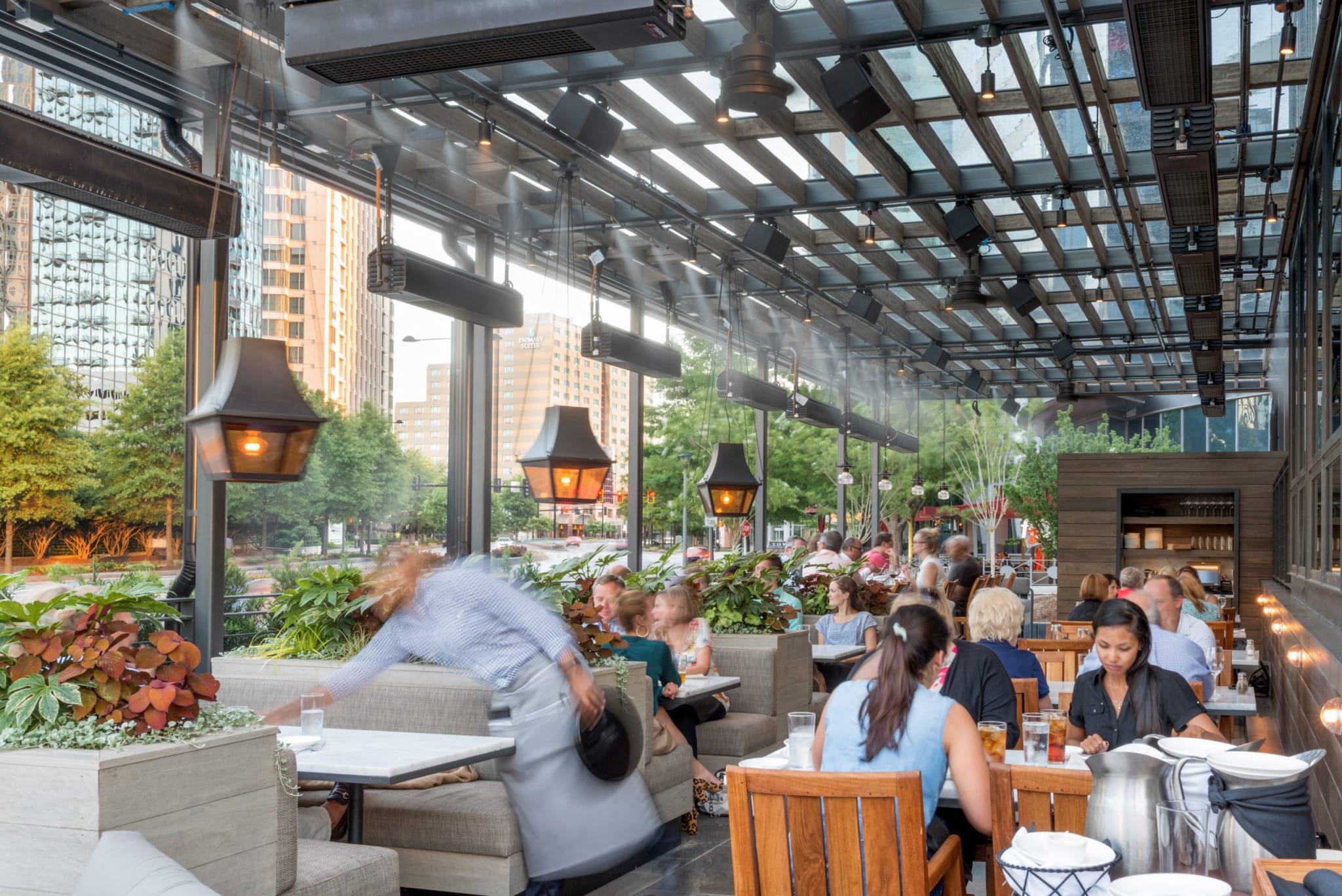 Patrons enjoy a meal at a bustling outdoor restaurant with a modern design and lush greenery in Atlanta, Georgia.