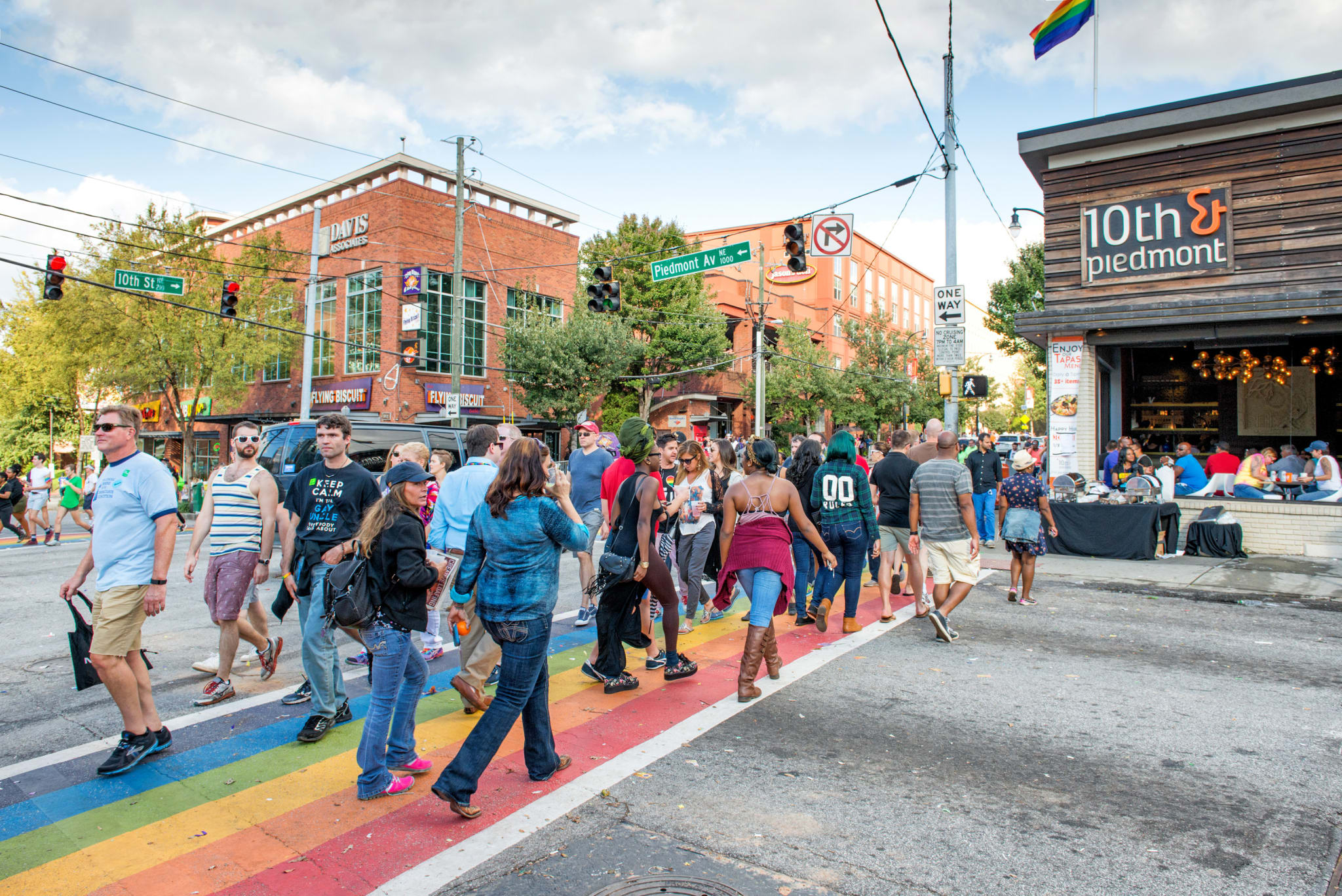 Crowd crossing rainbow-painted street during daytime parade or festival in Atlanta, Georgia.