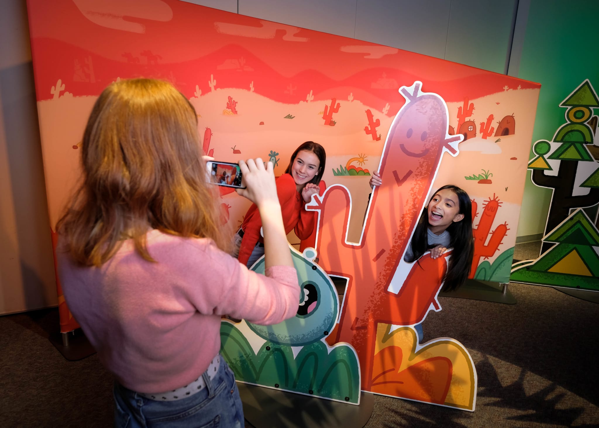 Three young girls pose for a photo with a large, colorful cactus cutout in a desert-themed room in Atlanta, Georgia.