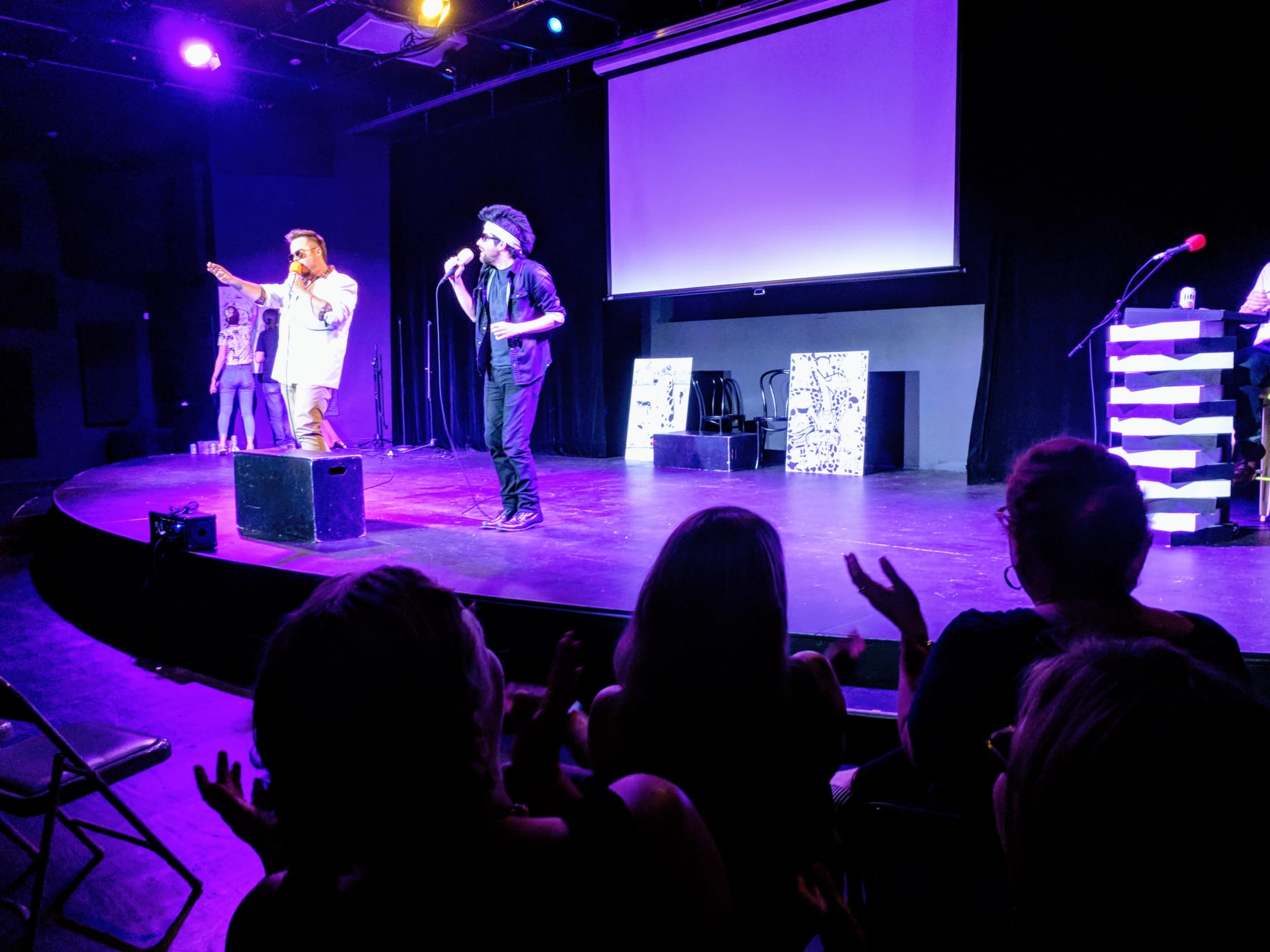 A group of performers on stage with microphones, engaging with an audience in a dimly lit theater in Atlanta, Georgia.