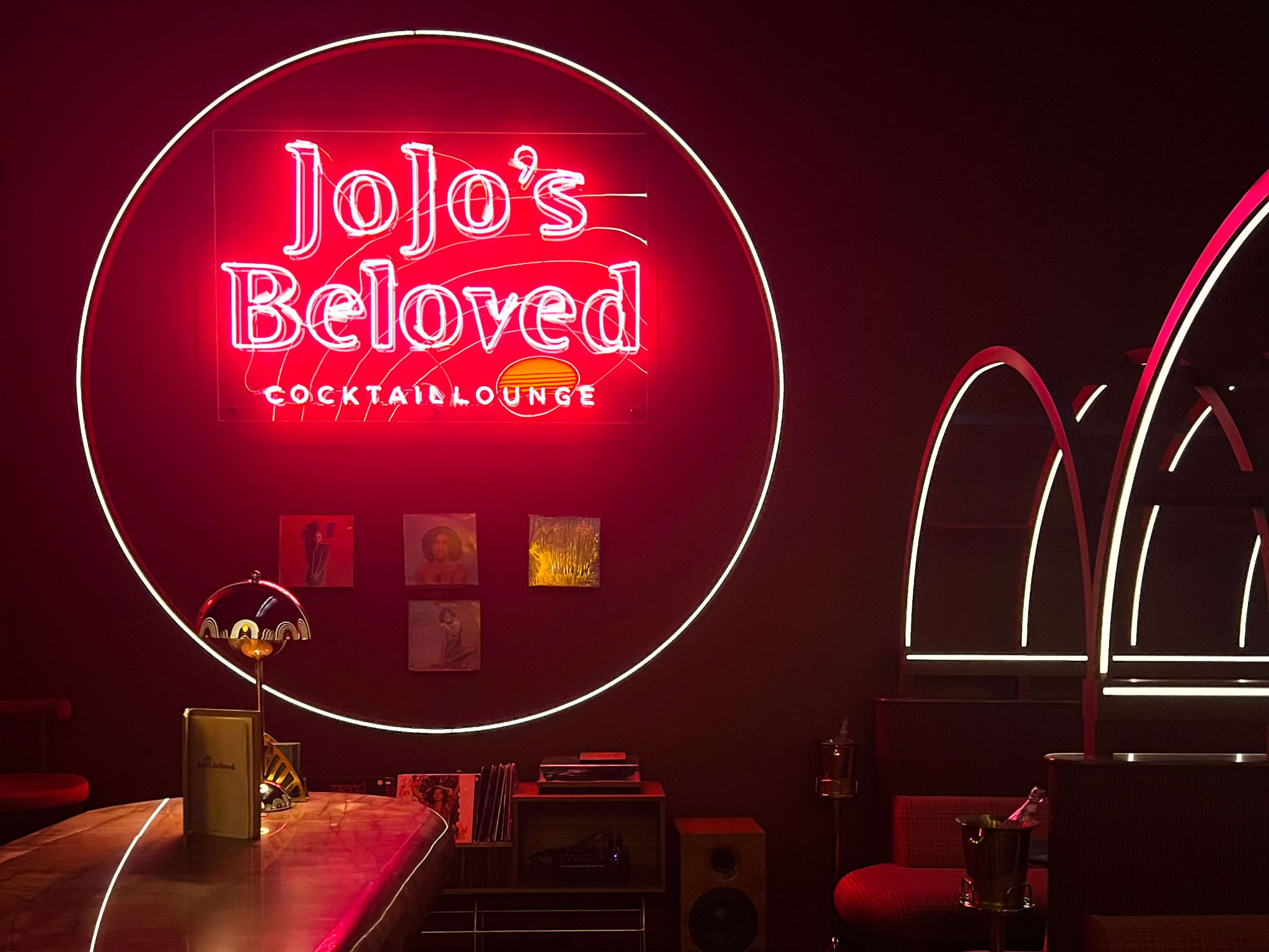 A dimly lit cocktail lounge with a prominent neon sign reading 'Jojo's Beloved' on the wall in Atlanta, Georgia.