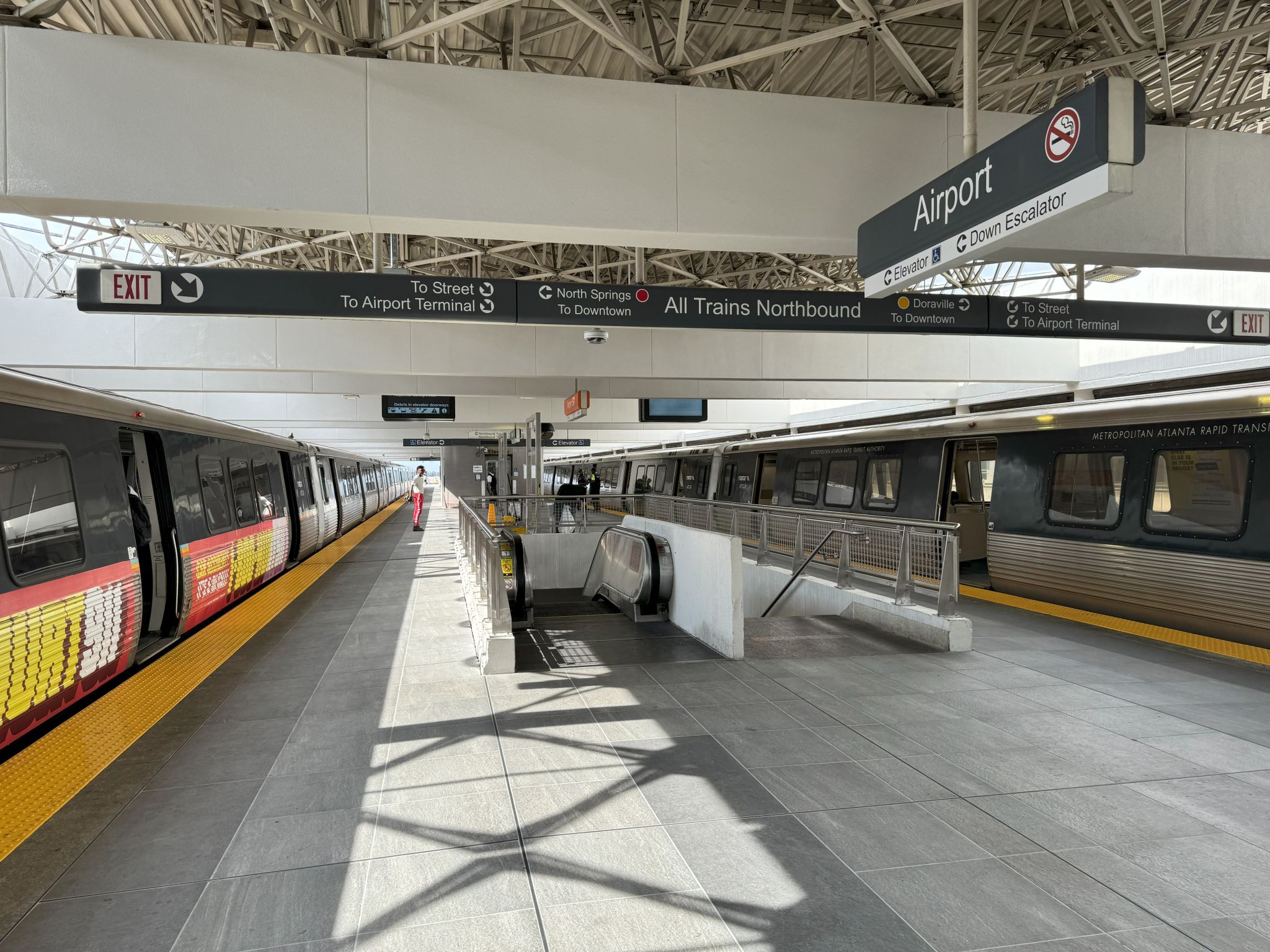 A modern train station with two trains, escalators, and clear signage in Atlanta, Georgia.