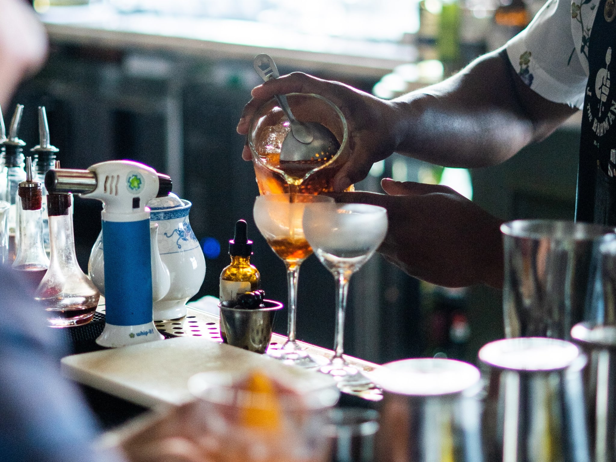 A bartender skillfully pours a golden liquid from a glass pitcher into a cocktail shaker in Atlanta, Georgia.