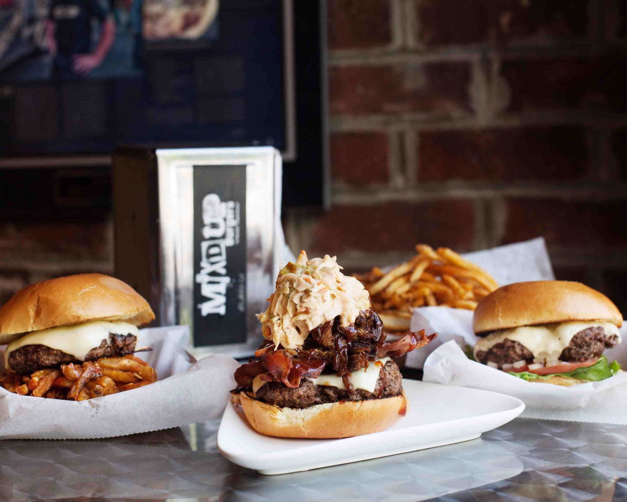 Three gourmet burgers with various toppings and sides of fries on a table in Atlanta, Georgia.