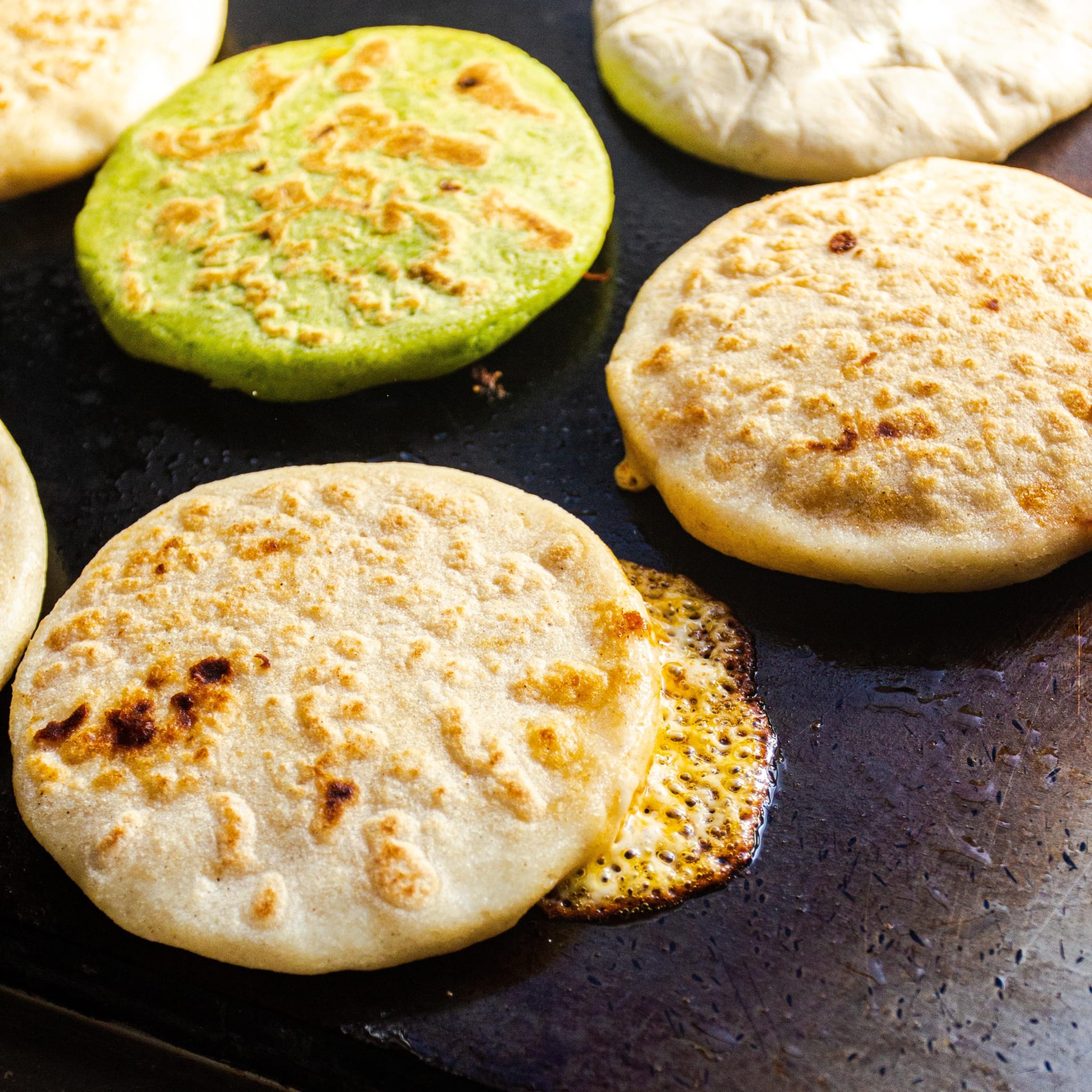 Several round, flatbread-like items cooking on a griddle, some with green coloring in Atlanta, Georgia.