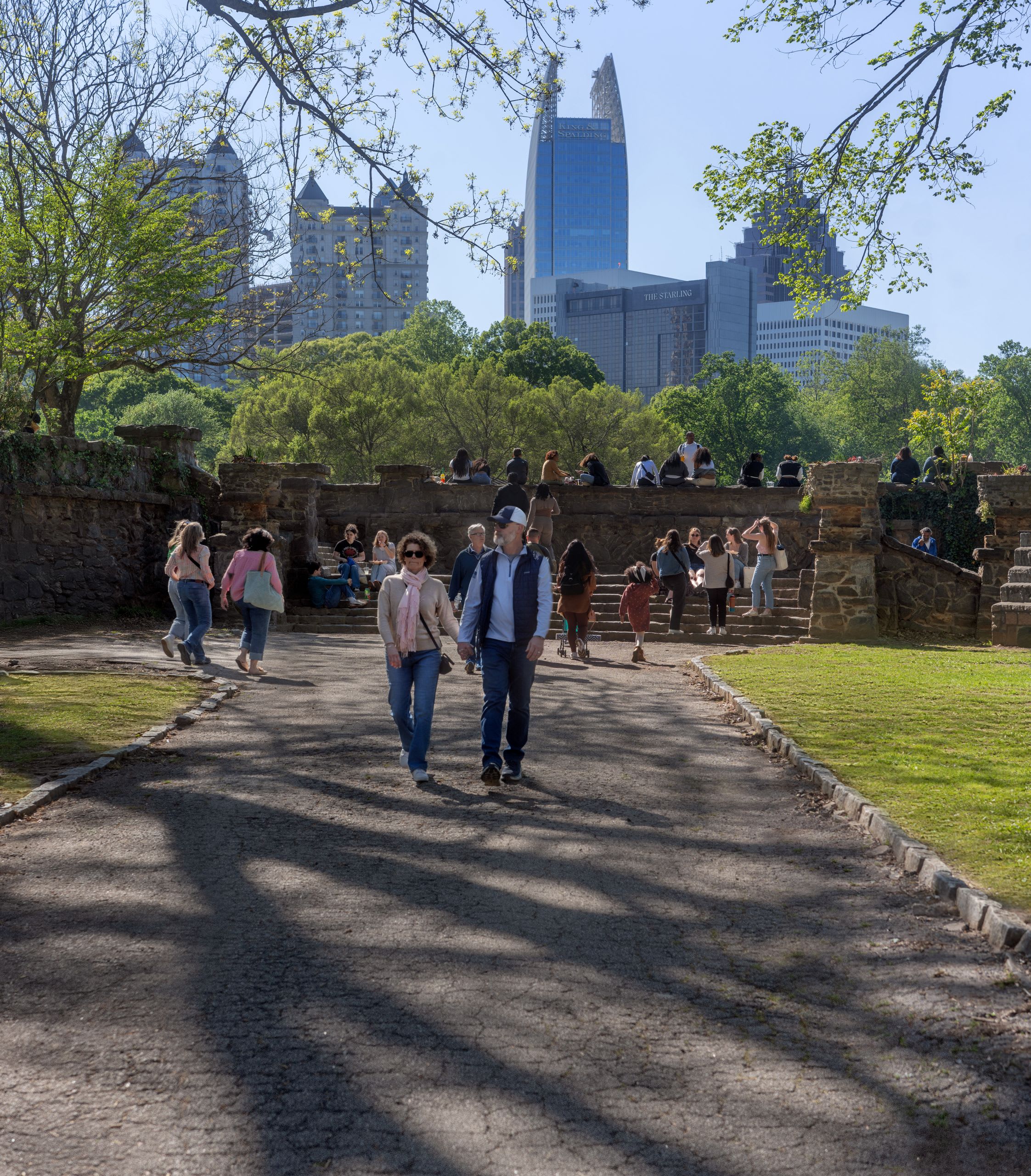 Piedmont Park 3 A sunny day in a city park with people walking on a path and sitting on stone walls in Atlanta, Georgia.