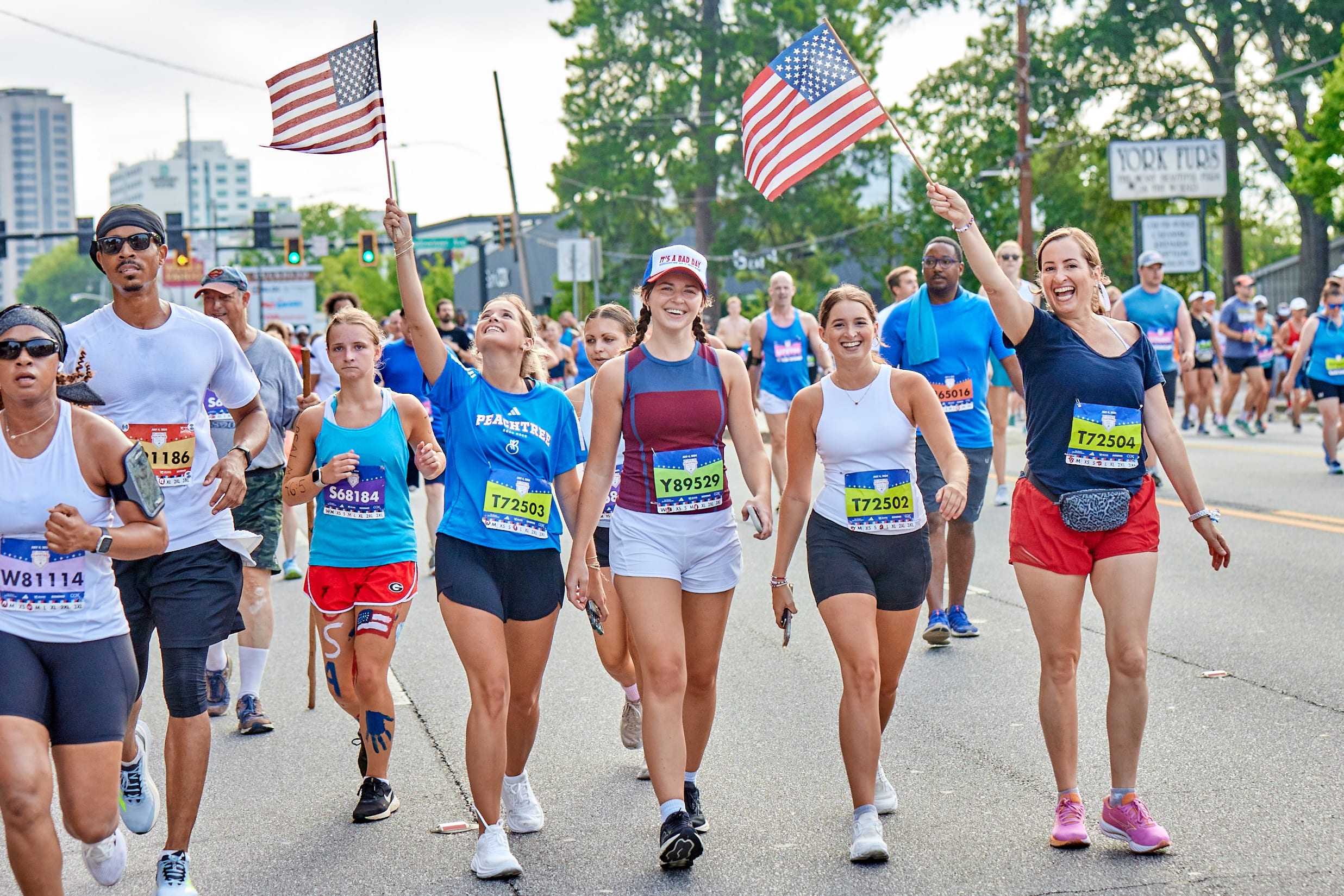 @DiscoverAtlanta Link In Bio 1 A group of runners, including women in athletic wear, carry American flags during a marathon in Atlanta, Georgia.