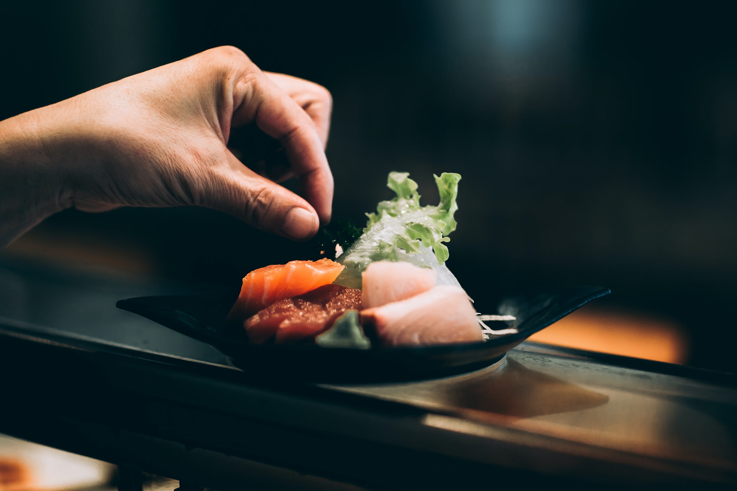 La Guía MICHELIN Regresa a Atlanta 2 A chef's hand carefully arranges colorful sashimi on a black plate with lettuce garnish in Atlanta, Georgia.