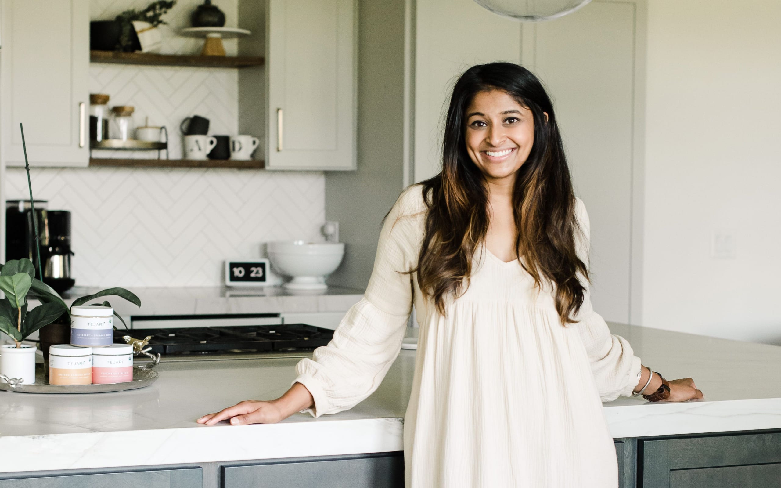 A woman in a white dress smiles in a modern kitchen with a marble countertop in Atlanta, Georgia.