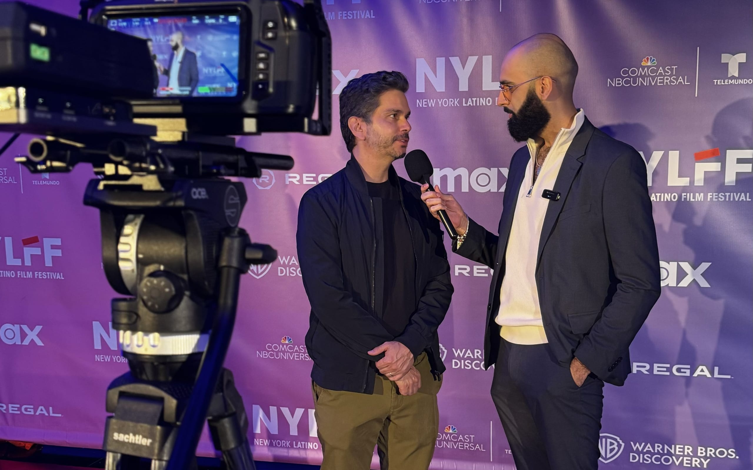 Two men in suits stand in front of a purple backdrop with logos, one holding a microphone in Atlanta, Georgia.