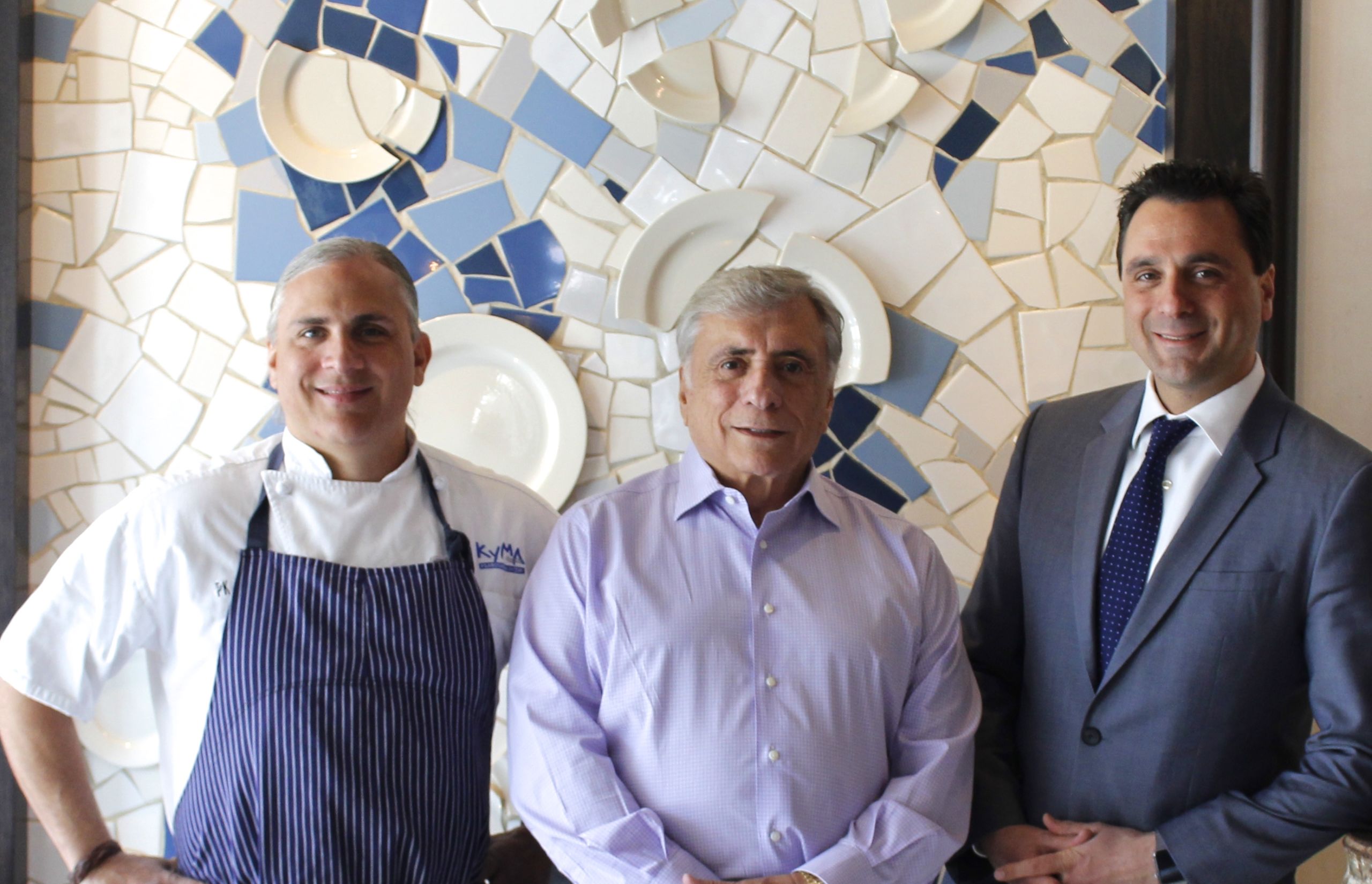 Three men posing. One in chef jacket and two in business attire. 