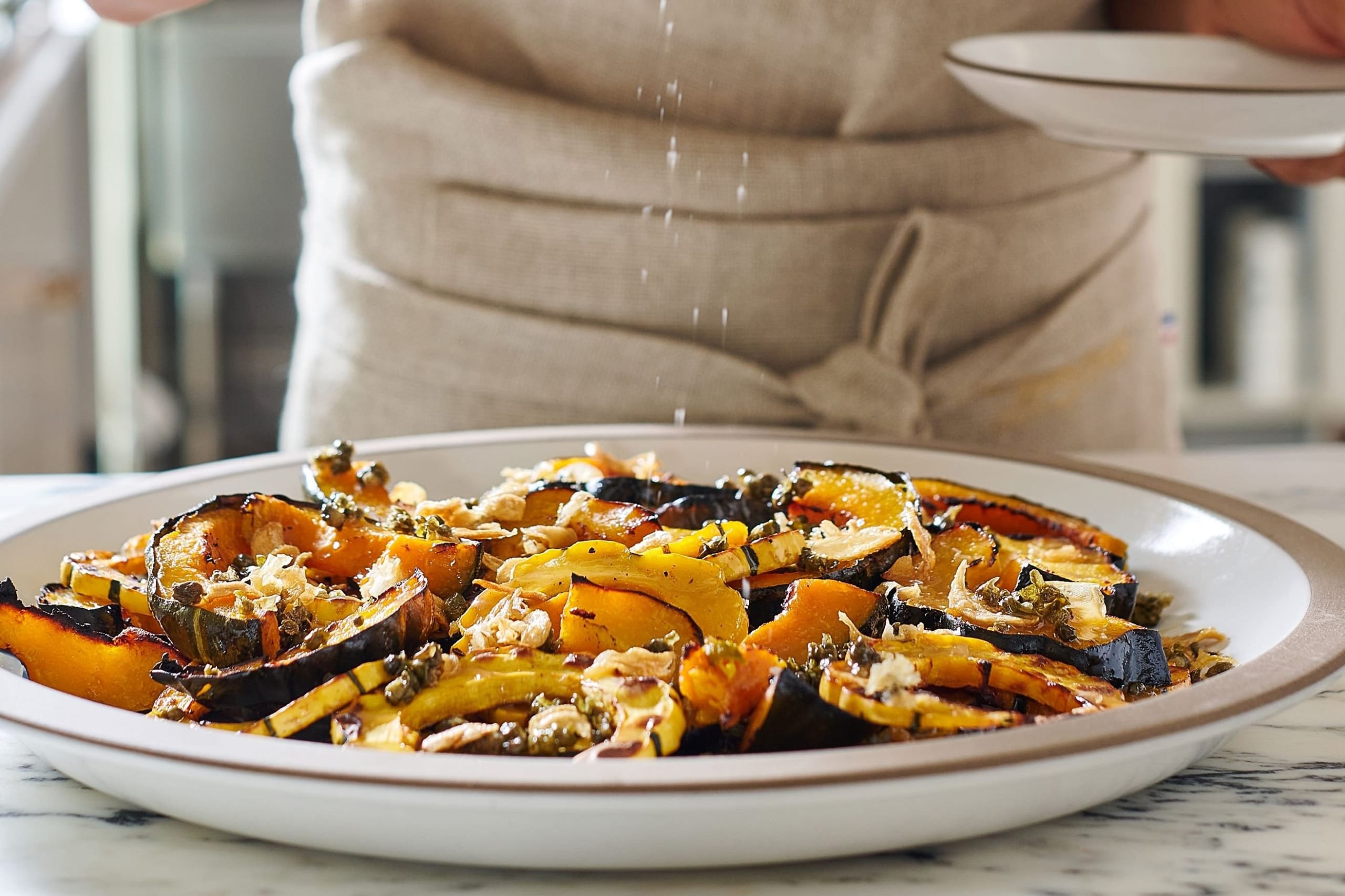 A chef sprinkles salt on a plate of roasted butternut squash slices in Atlanta, Georgia.