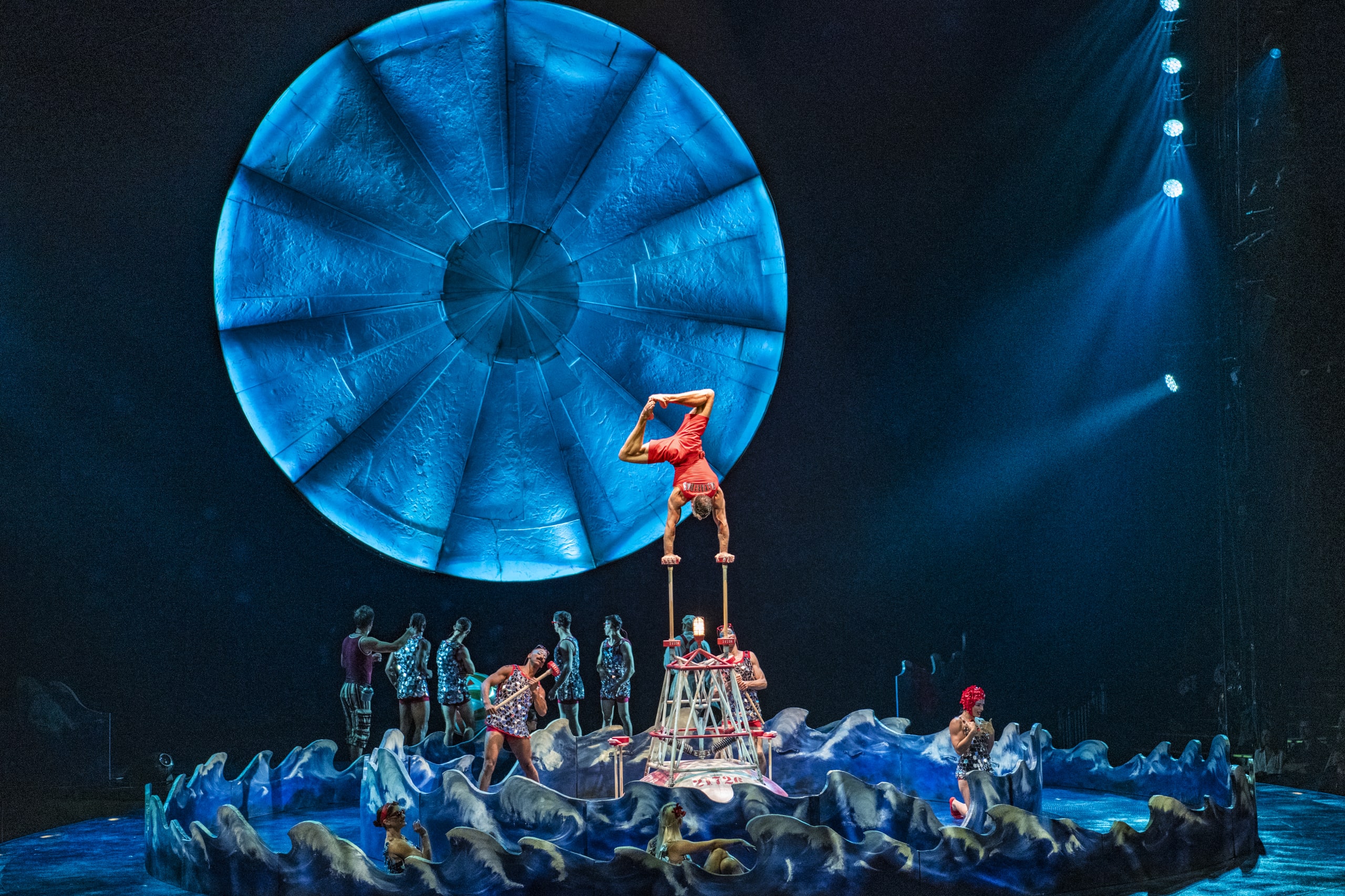 A circus performer balances on two poles while others stand on a wave-like platform below in Atlanta, Georgia.