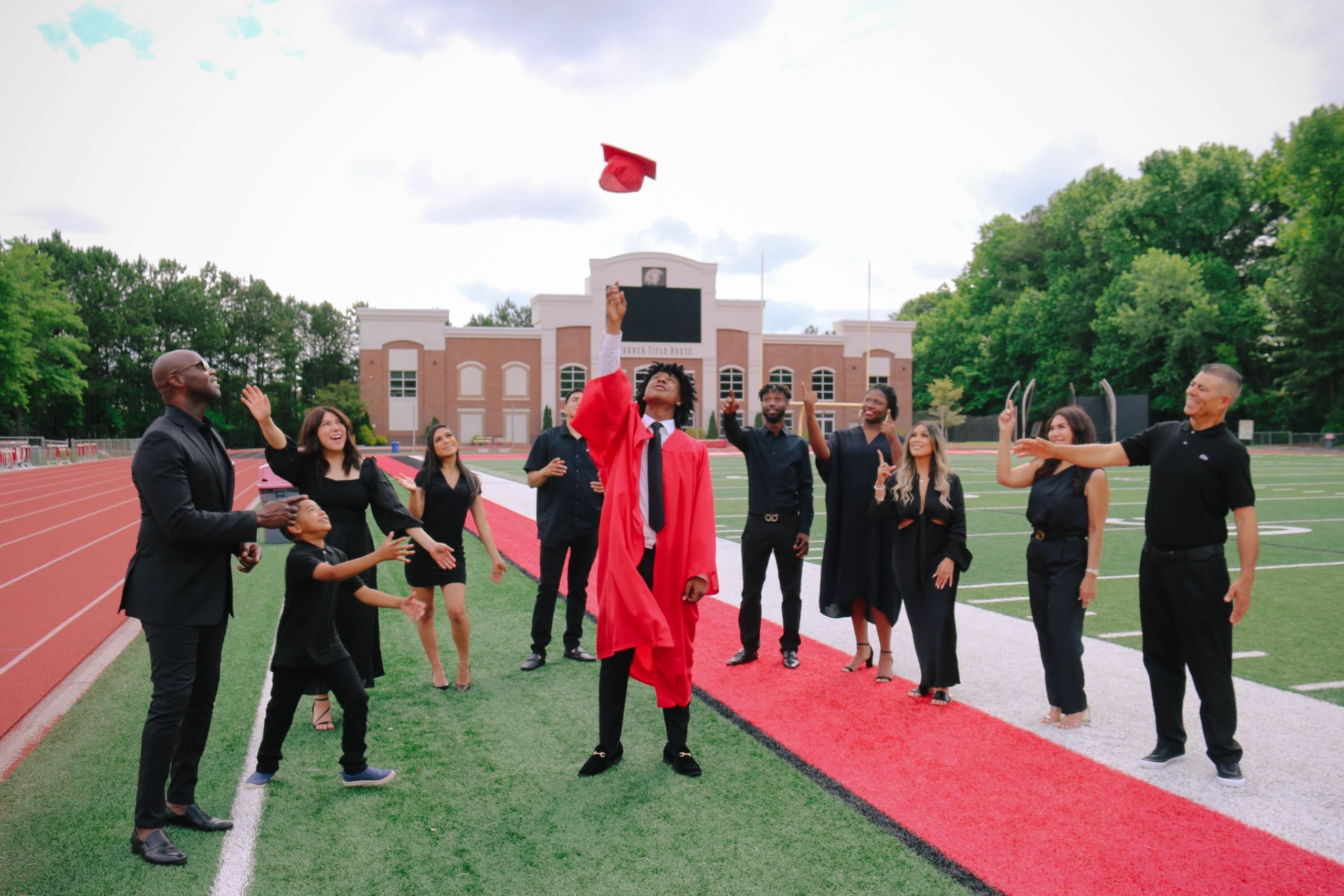 @DiscoverAtlanta Link In Bio 115 Graduates in black and red gowns celebrate on a football field with a building in the background in Atlanta, Georgia.