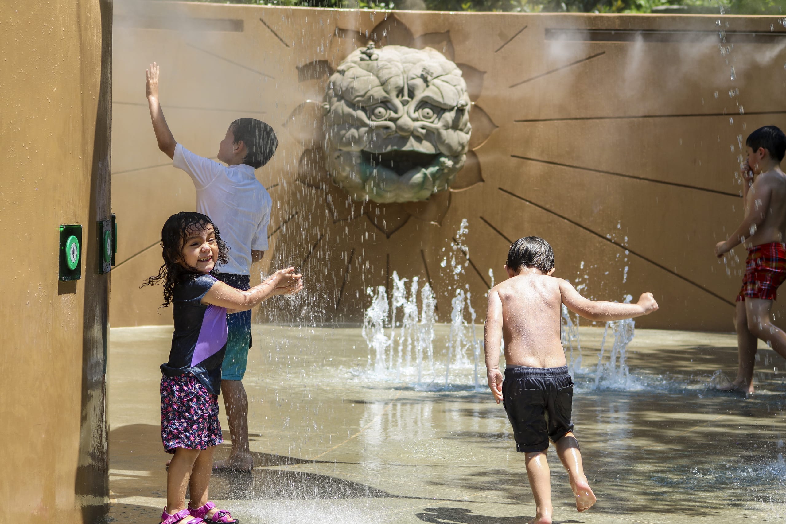 Children playfully splash in a water park, surrounded by decorative fountains and sculptures in Atlanta, Georgia.