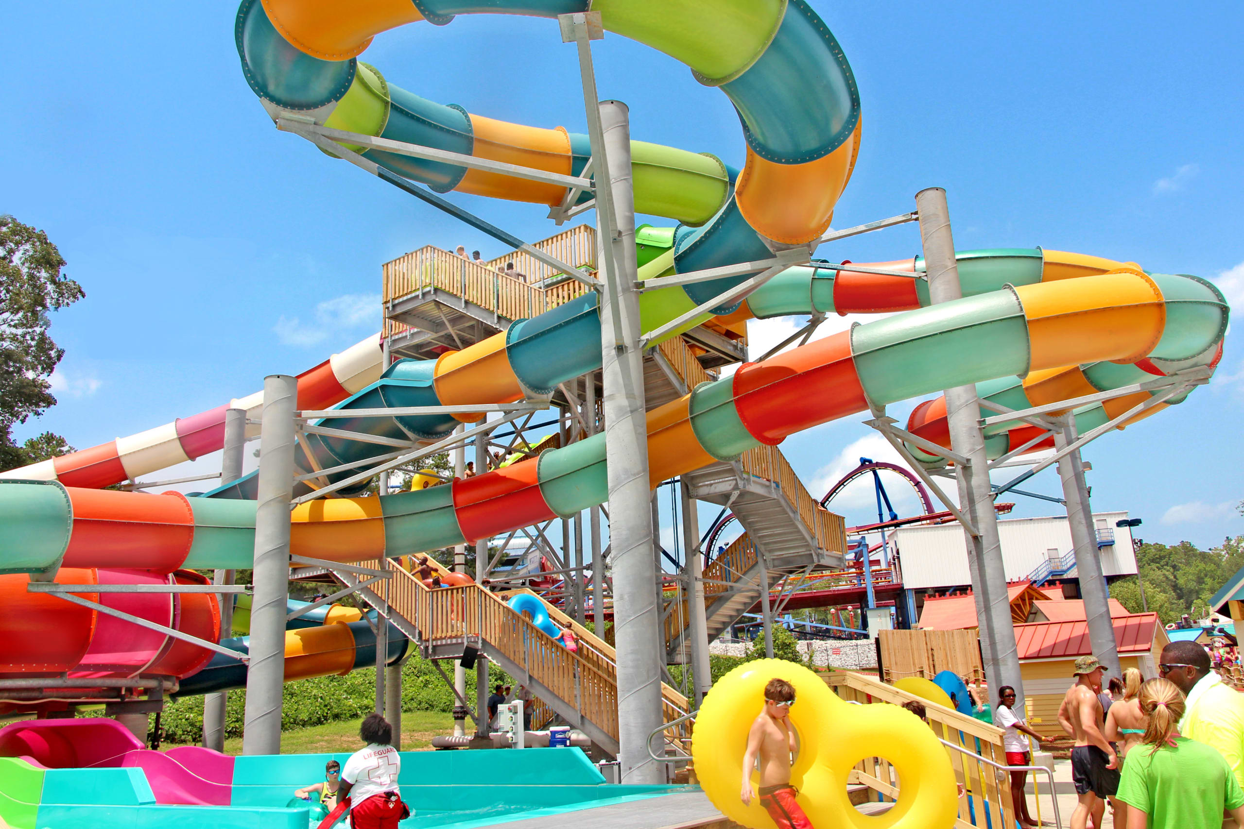 A vibrant water park features a towering, colorful water slide with multiple loops and a crowded pool area in Atlanta, Georgia.