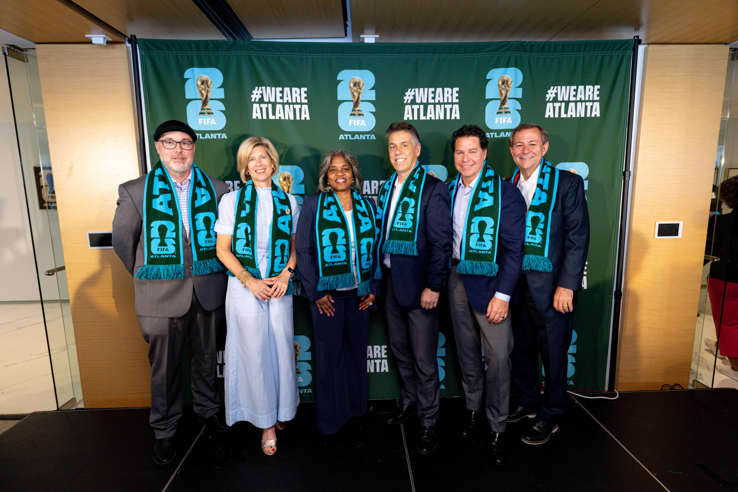 Atlanta Marks One Year to Go until the FIFA World Cup 26™ with Joint Host City Efforts and Citywide Celebrations 1 Six people stand together wearing matching scarves in front of a green banner in Atlanta, Georgia.