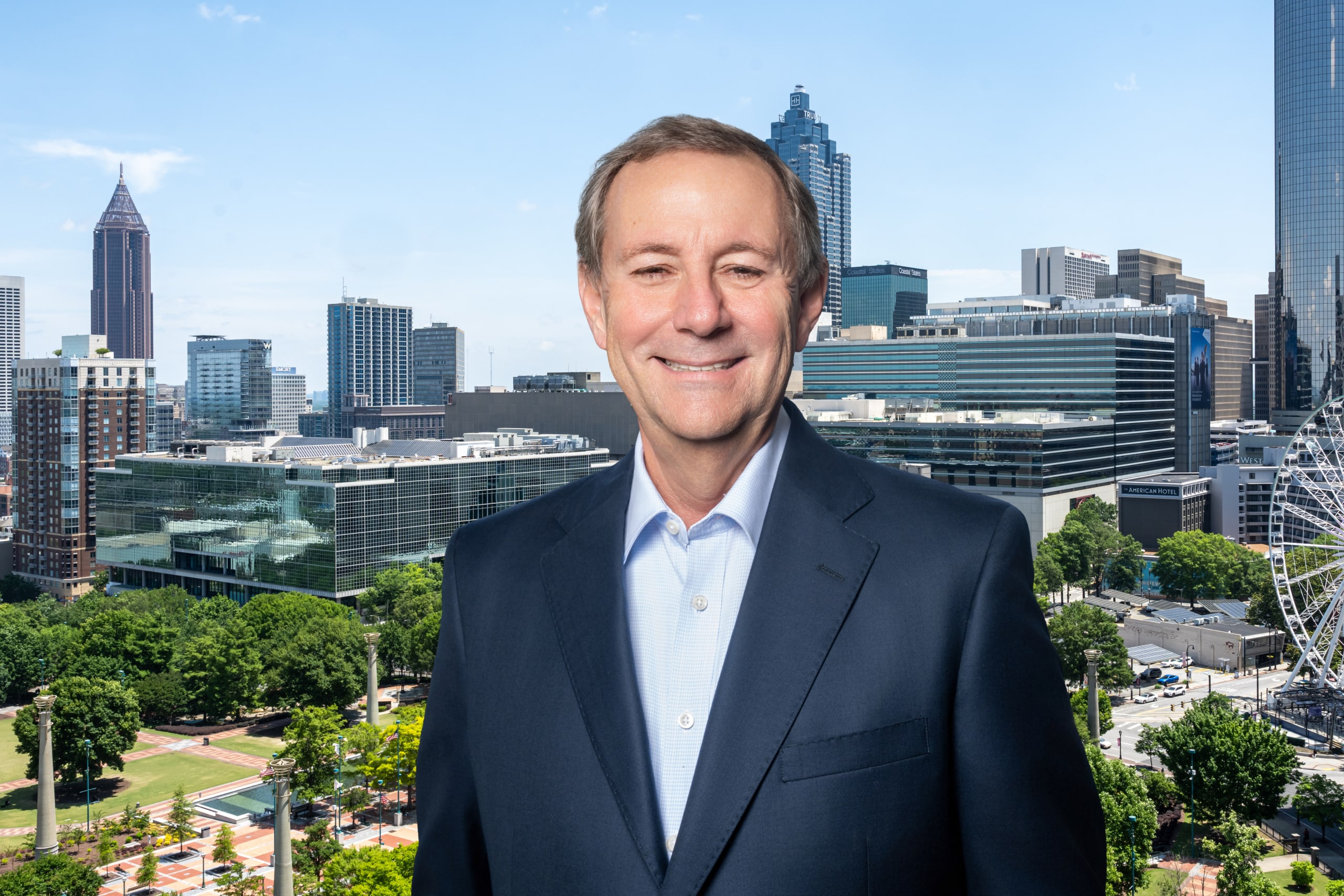 William Pate A smiling man in a suit stands in front of a city skyline with a Ferris wheel in Atlanta, Georgia.