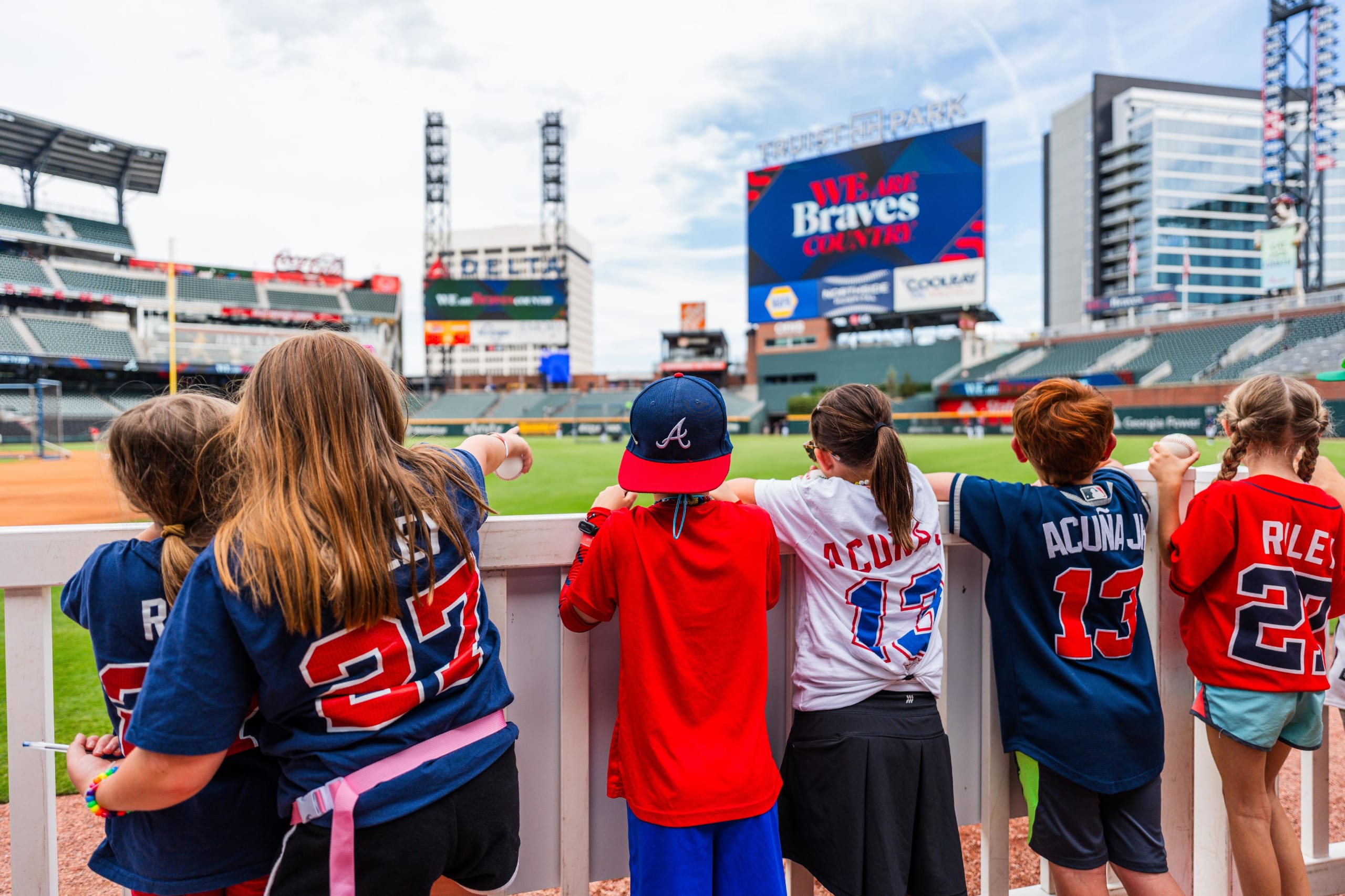 Children in baseball jerseys stand together, watching a game at a stadium in Atlanta, Georgia.