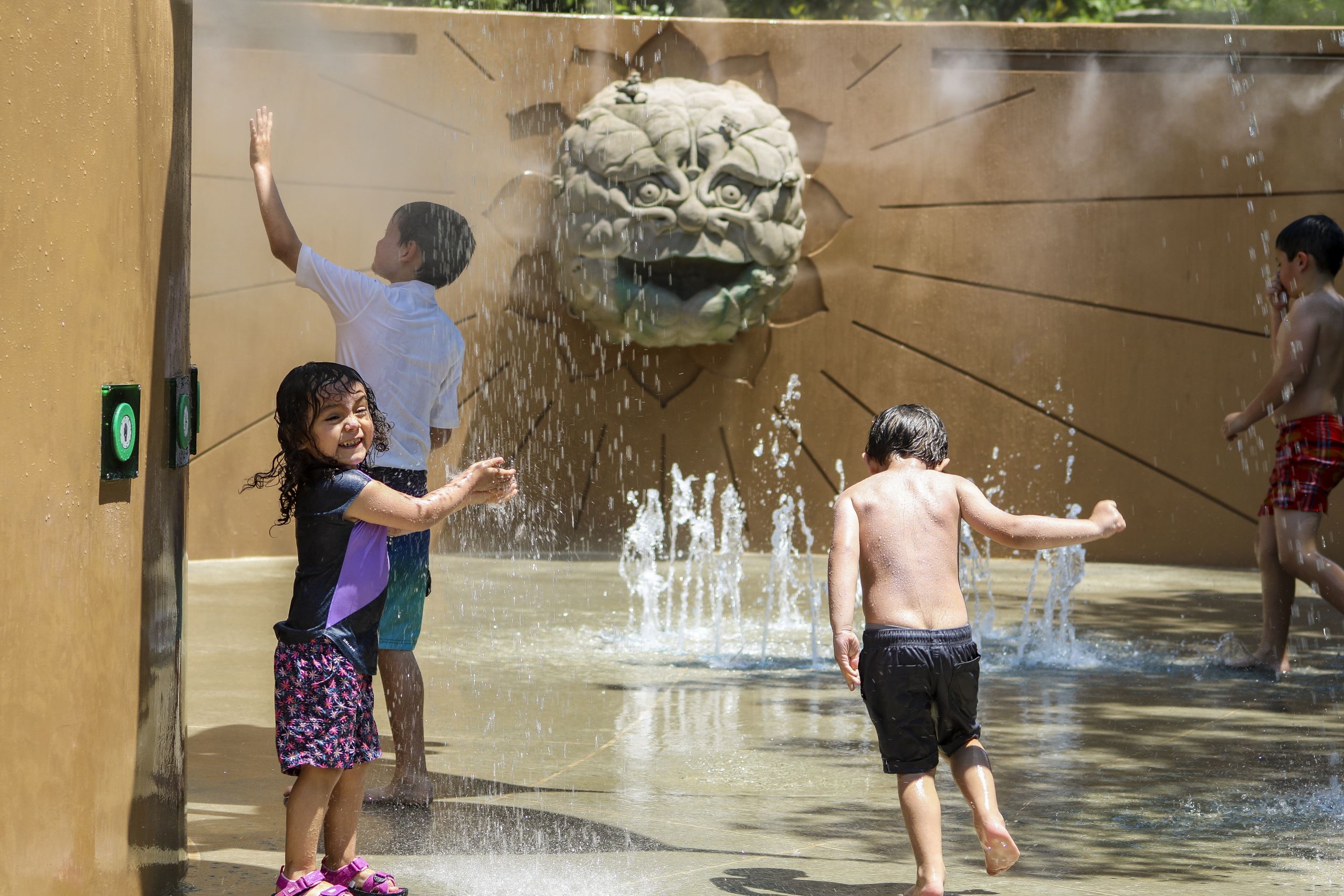 Children playfully splash in a water park, surrounded by decorative fountains and sculptures in Atlanta, Georgia.