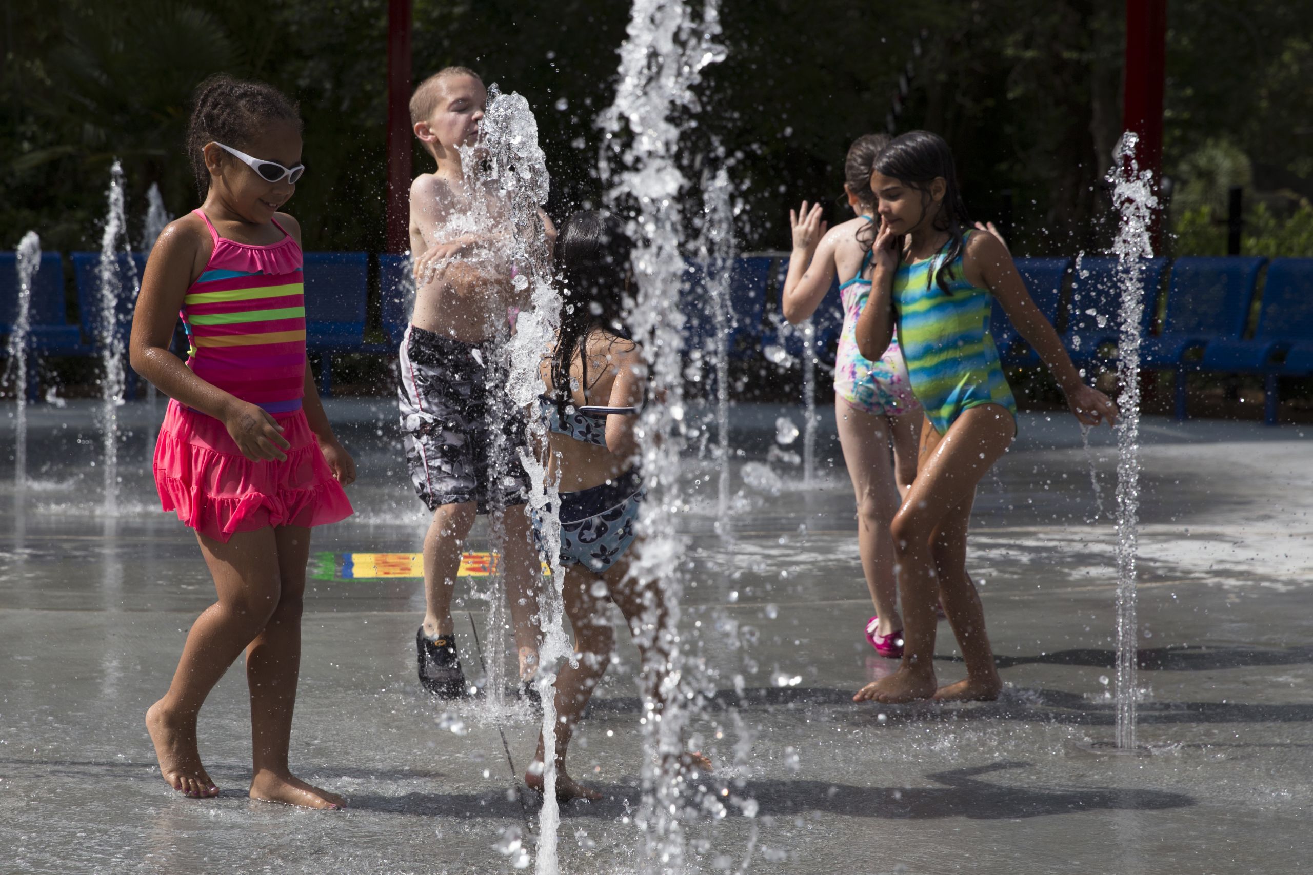 Children in colorful swimsuits playfully splash in a public water fountain on a sunny day in Atlanta, Georgia.
