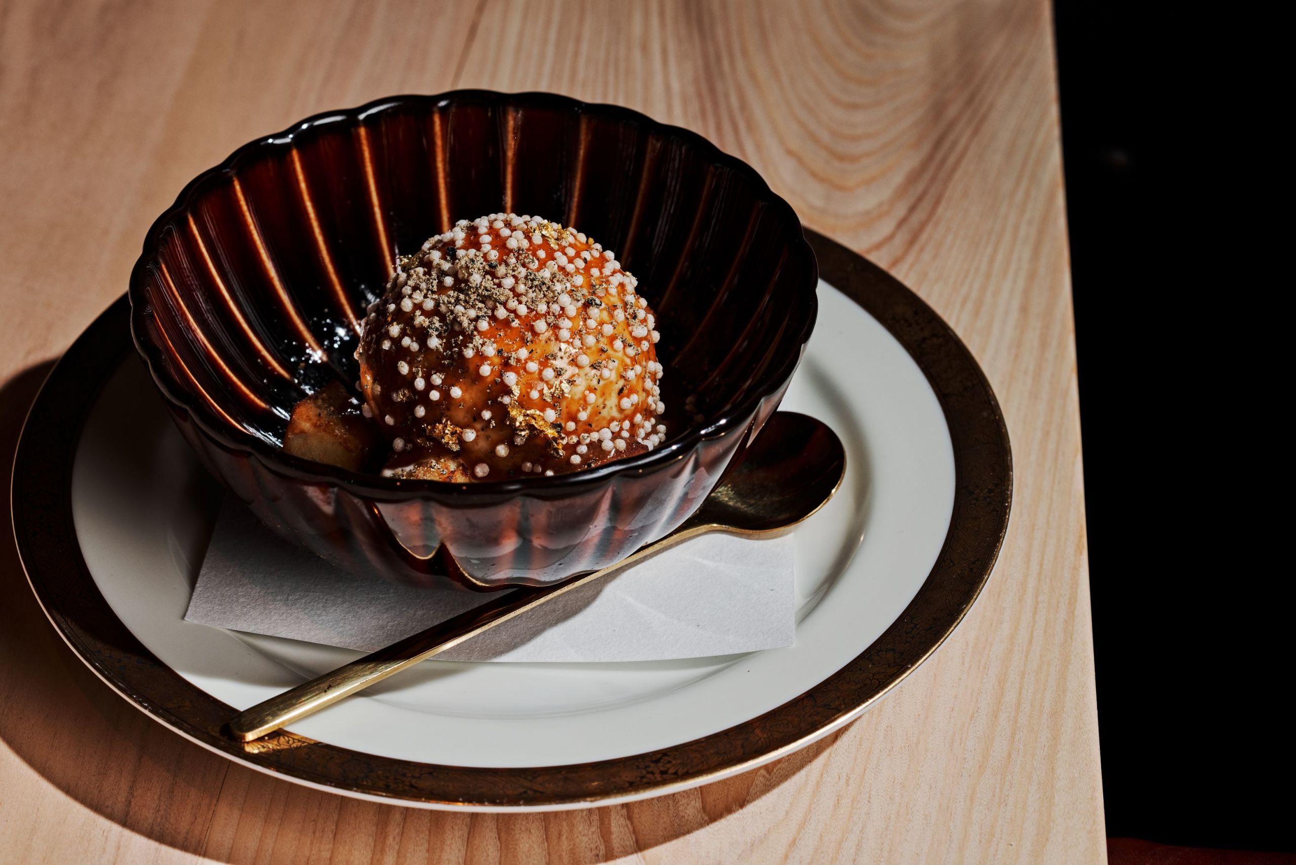Where to Dine with a Large Group at Atlanta’s Michelin Guide Restaurants 4 A dark brown, fluted bowl with a golden rim holds a golden-brown dessert ball sprinkled with white and black toppings in Atlanta, Georgia.