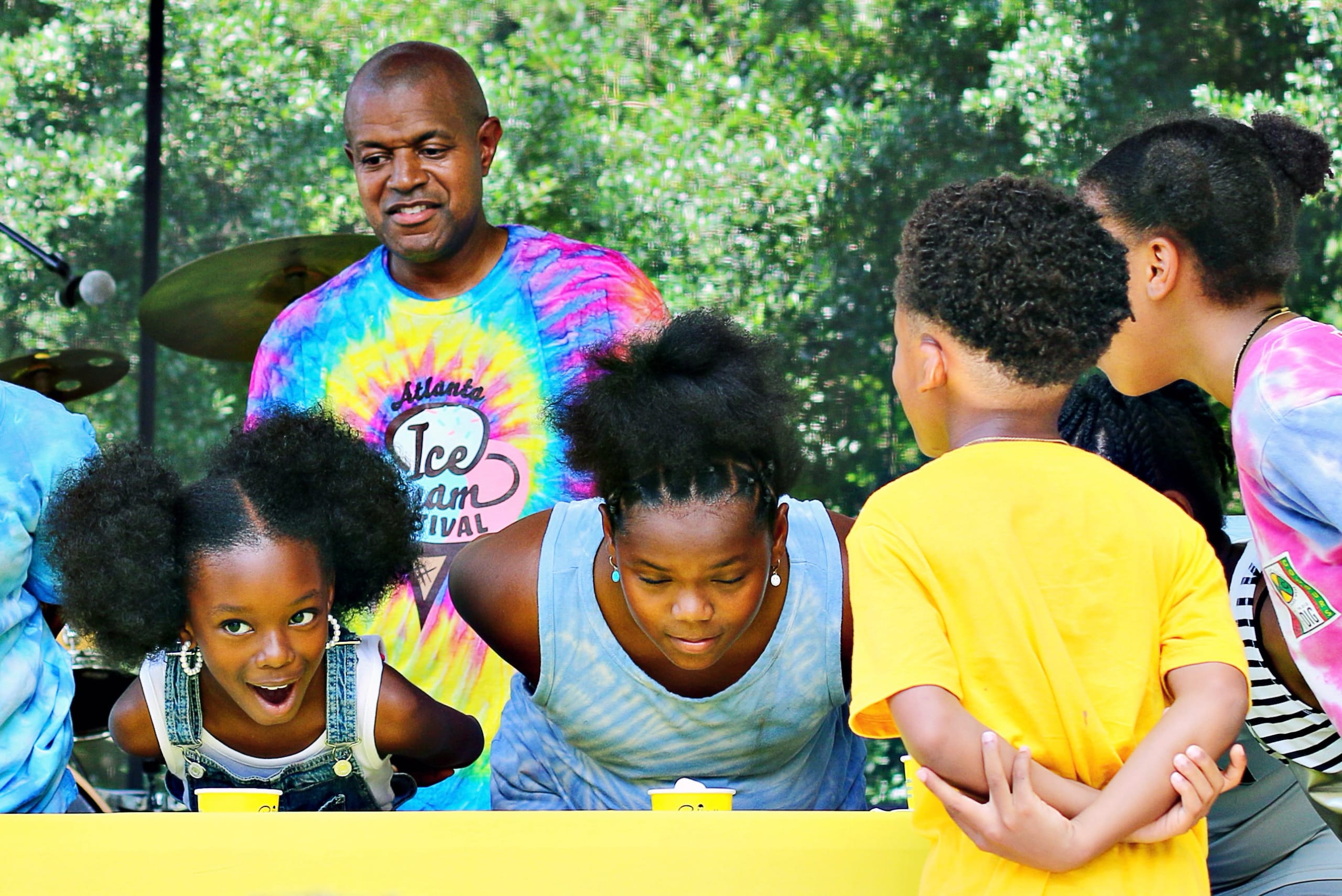 A group of children and an adult are gathered around a table, engaged in an activity at an outdoor event in Atlanta, Georgia.