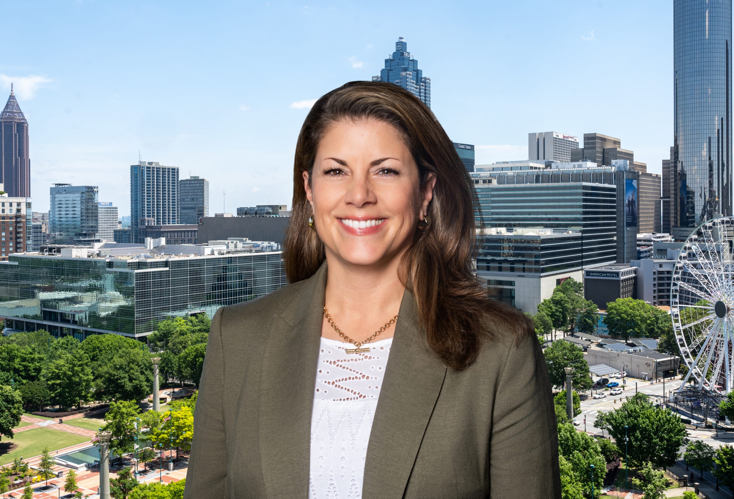 A woman in a green blazer smiles in front of a city skyline with skyscrapers and a Ferris wheel in Atlanta, Georgia.