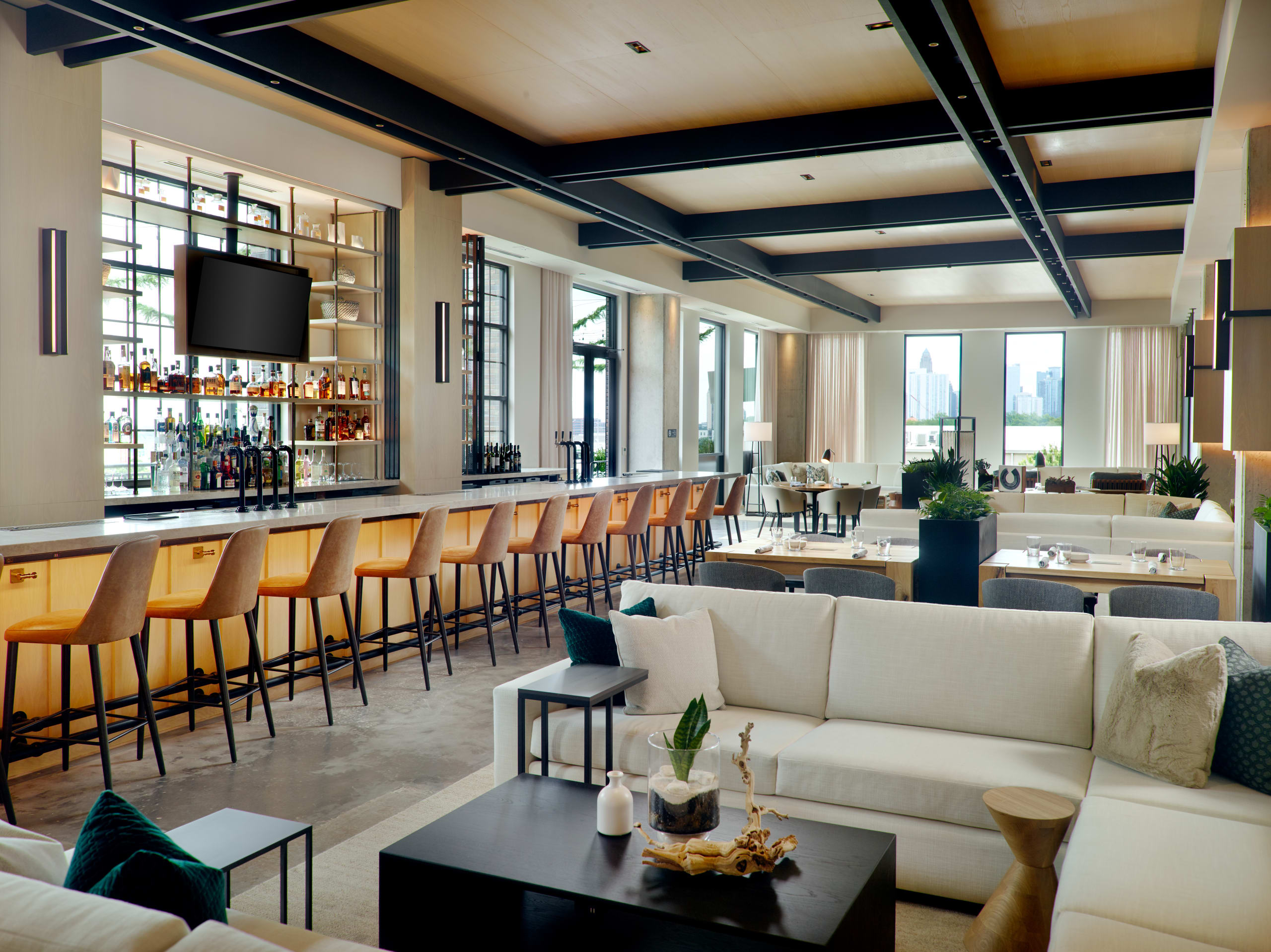 Modern, spacious bar and lounge area with white sofas, orange chairs, and a large TV in Atlanta, Georgia.