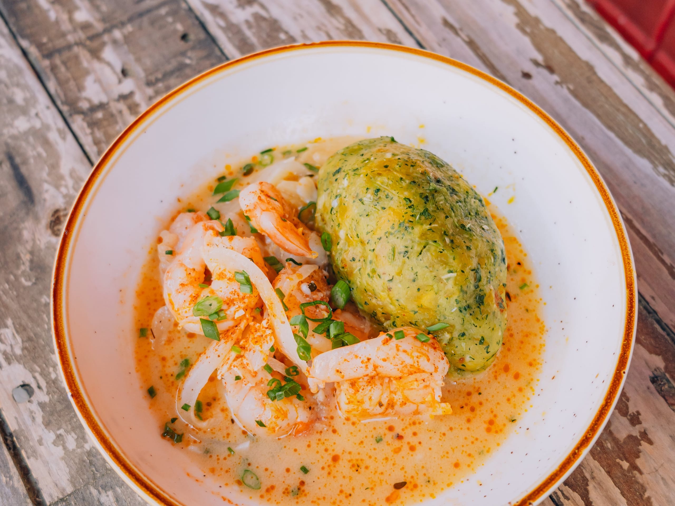 A bowl of creamy orange soup with shrimp, green dumplings, and chopped herbs in Atlanta, Georgia.