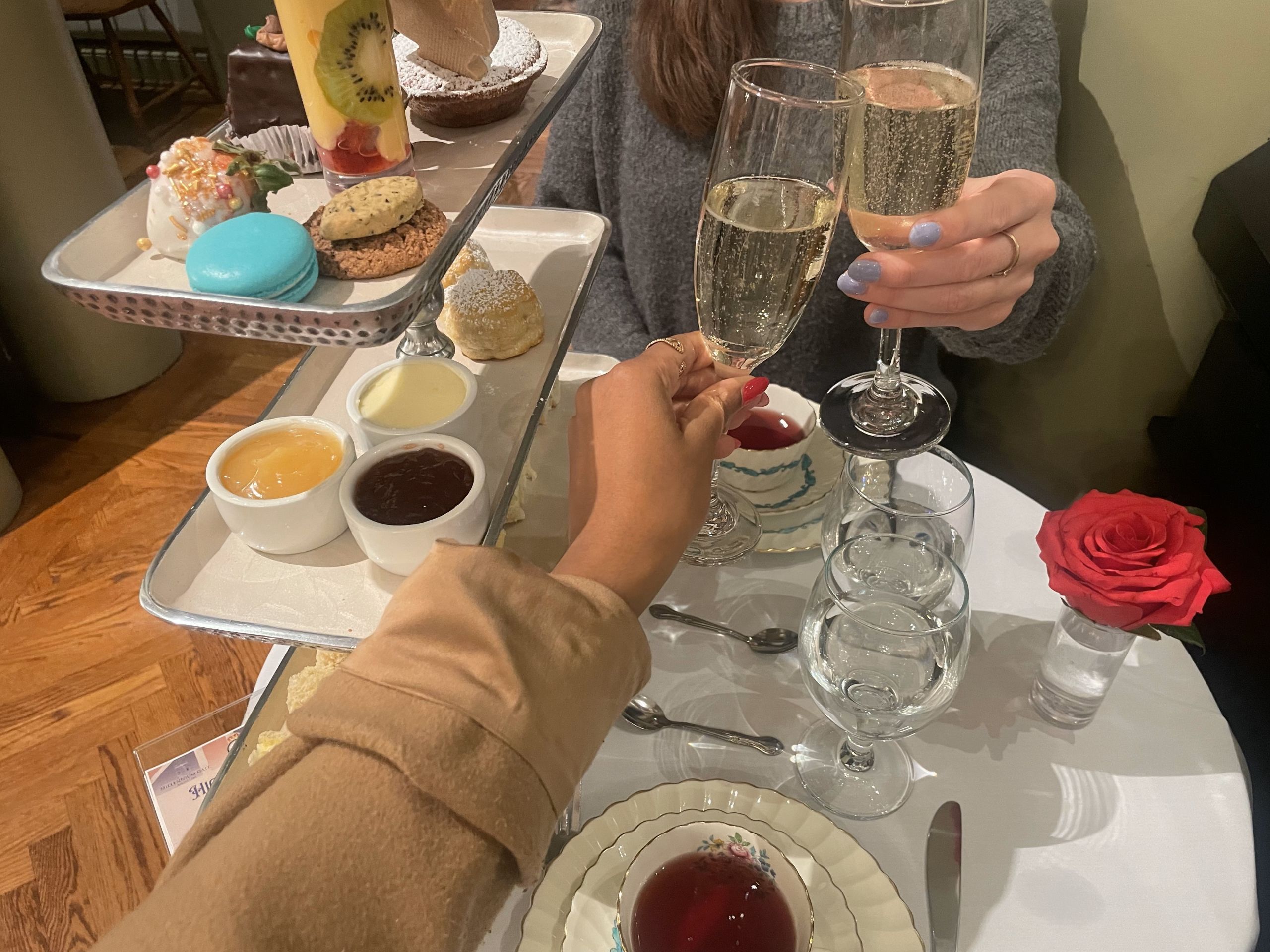Two women clink champagne glasses at a high tea table with pastries and desserts in Atlanta, Georgia.