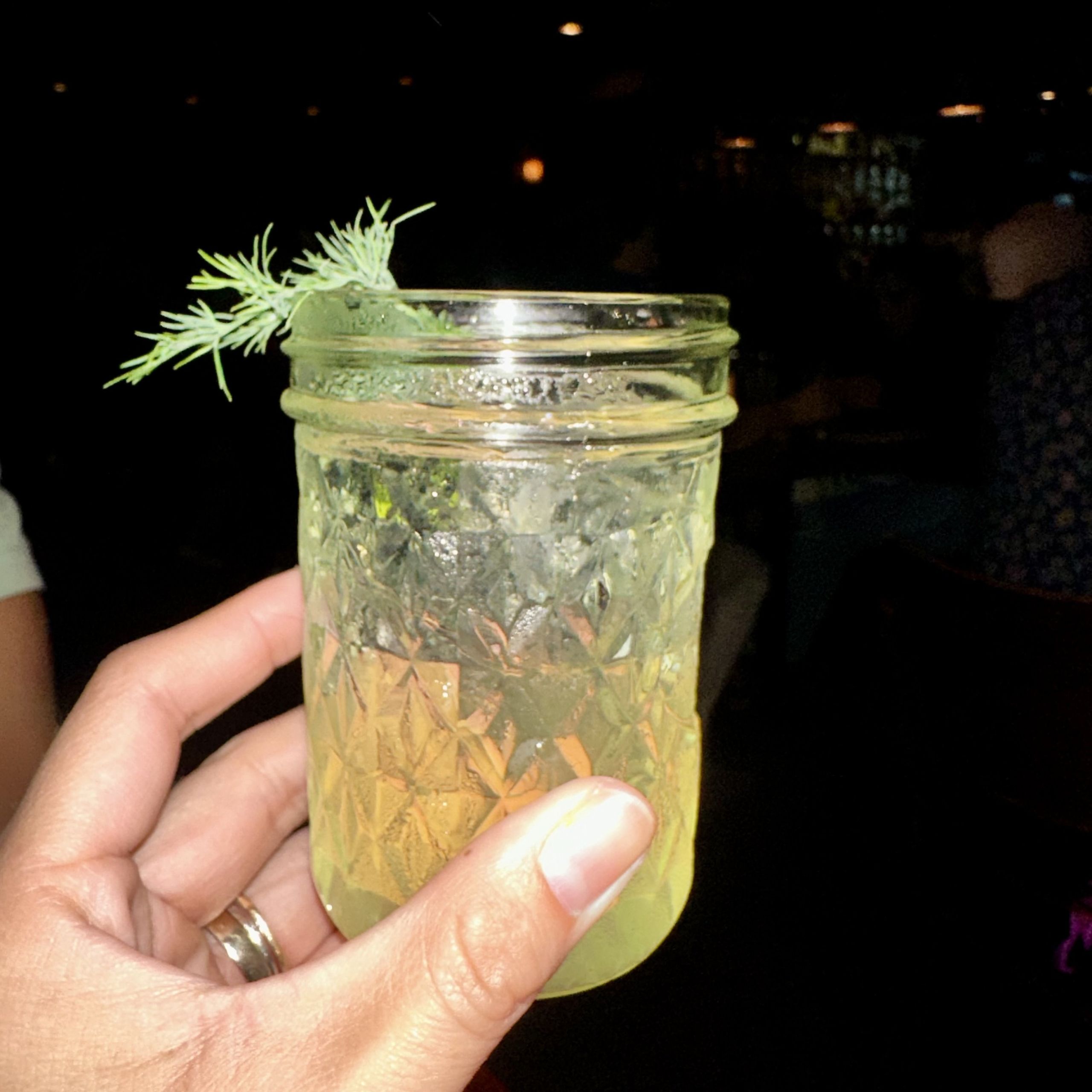 Must-Try Summer Cocktails in Atlanta 4 A hand holds a frosty mason jar filled with a yellow liquid and garnished with dill in Atlanta, Georgia.