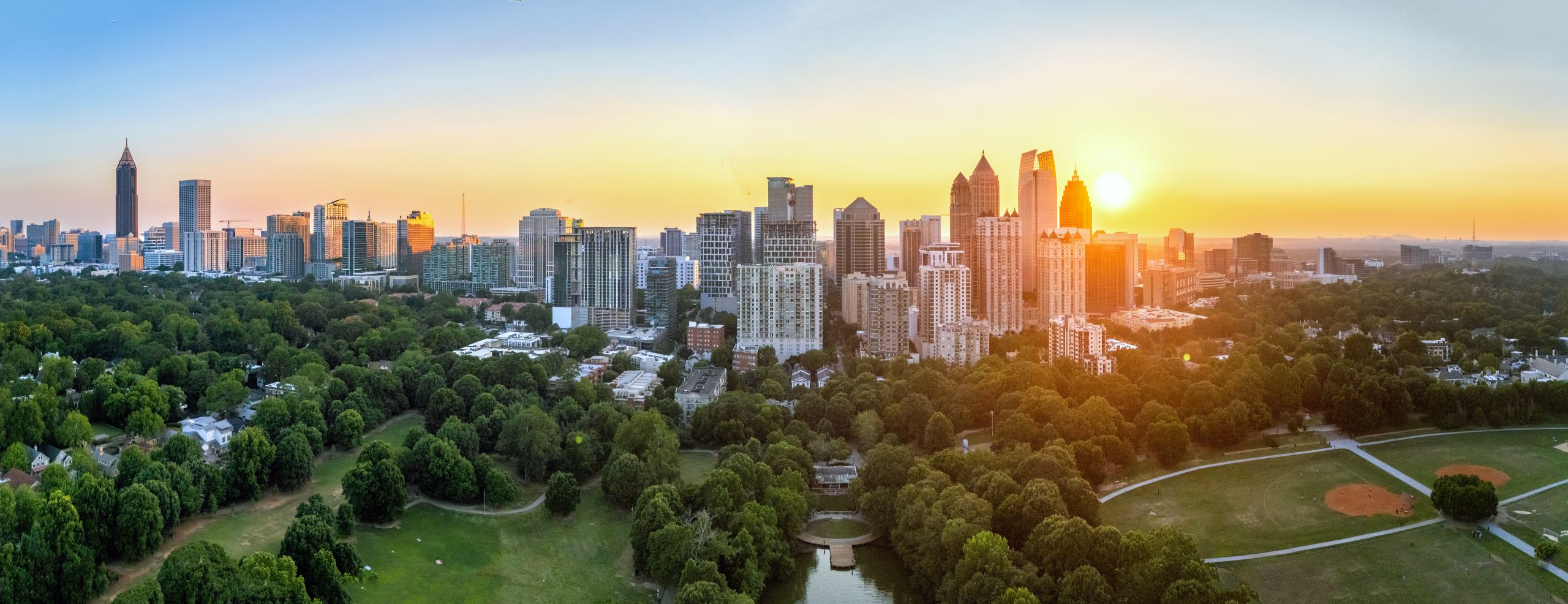 Piedmont Park 1 Aerial view of a sprawling city skyline at sunset, surrounded by lush green parks and fields in Atlanta, Georgia.