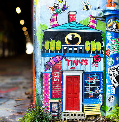 Karen Anderson 1 Colorful mural of a whimsical house with a red door and various stickers on a utility box in Atlanta, Georgia.