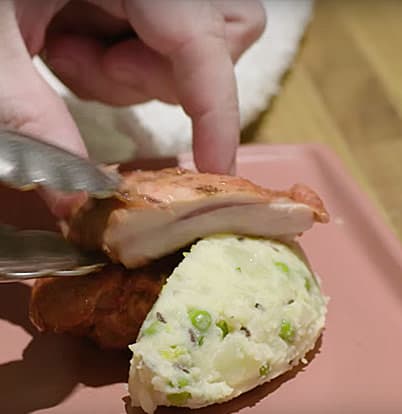 Chef Kevin Gillespie 2 A hand uses tongs to stack mashed potatoes with peas and grilled chicken on a plate in Atlanta, Georgia.