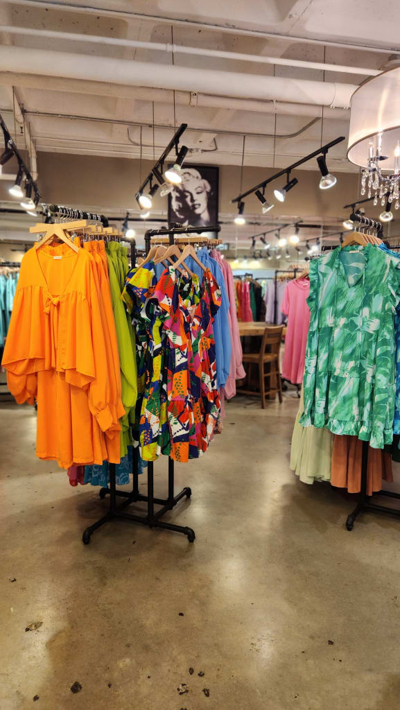 How to Shop at AmericasMart Atlanta 1 A brightly lit clothing store displays colorful dresses and tops on racks in Atlanta, Georgia.