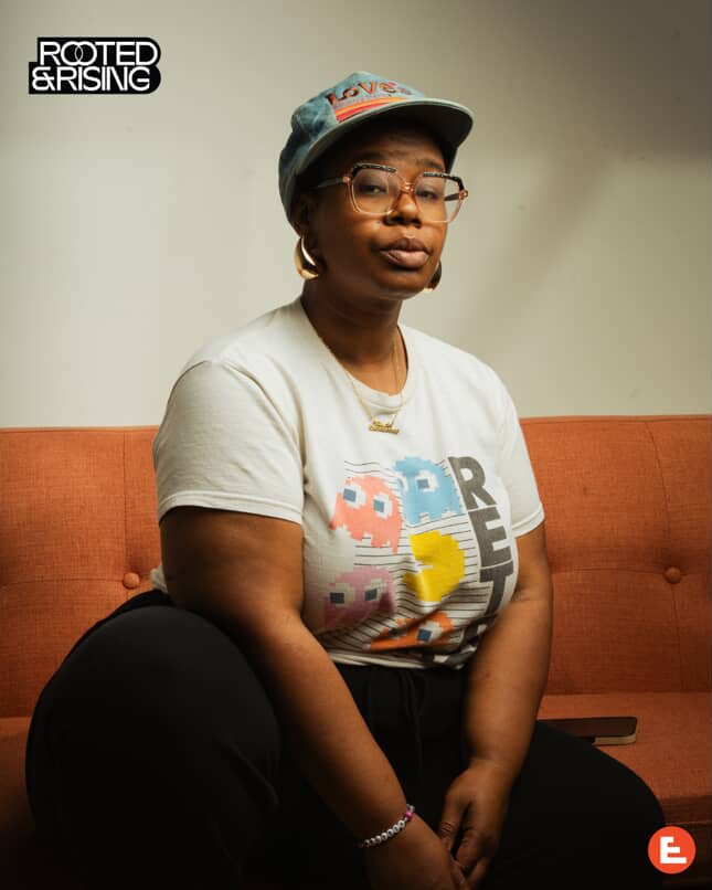 Elevate 2025: Art, Music, Fashion 4 A woman sits on a red couch wearing a white t-shirt with Pac-Man characters and a blue cap in Atlanta, Georgia.