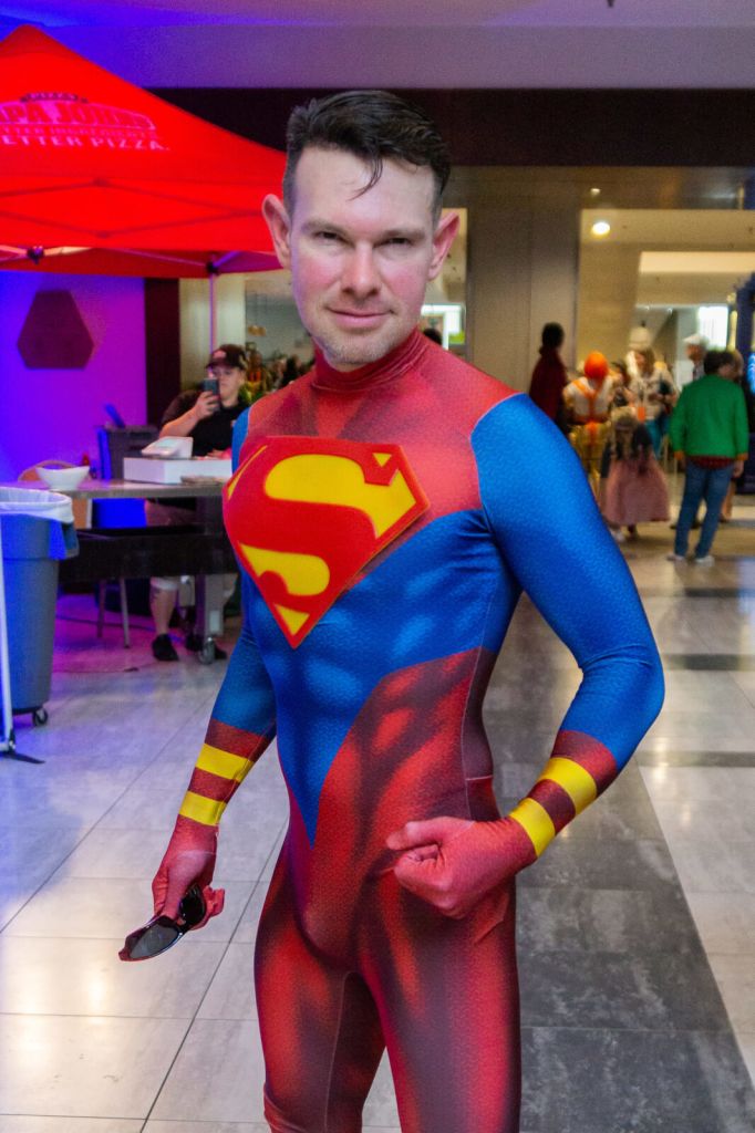 Fun Facts About Dragon Con that you Probably Didn’t Know 1 A muscular man in a red and blue Superman costume stands confidently in a convention center in Atlanta, Georgia.