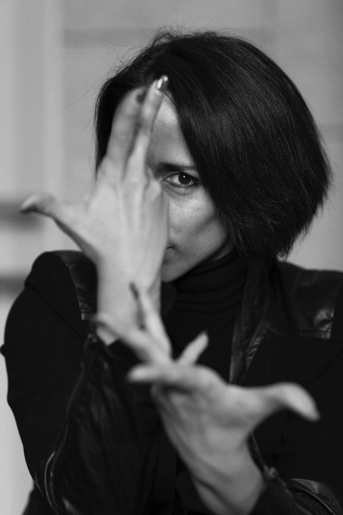 A woman with short dark hair is striking a dramatic pose with her hands, wearing a black leather jacket in Atlanta, Georgia.