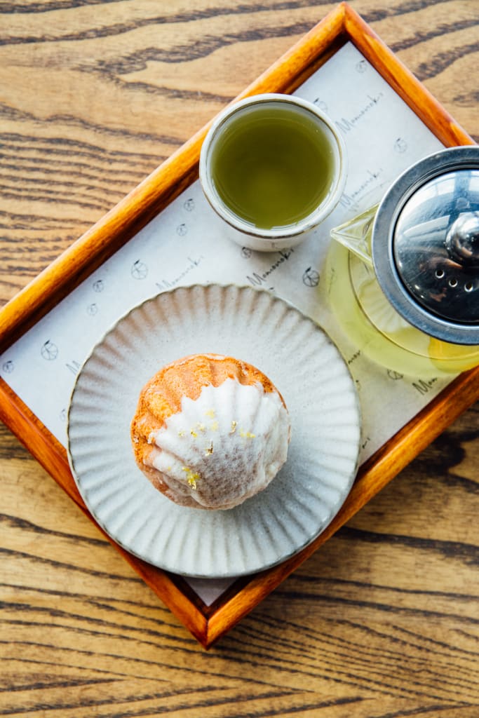 A wooden tray holds a green tea pot, a cup of green tea, and a scalloped plate with a pastry dusted with powdered sugar in Atlanta, Georgia.