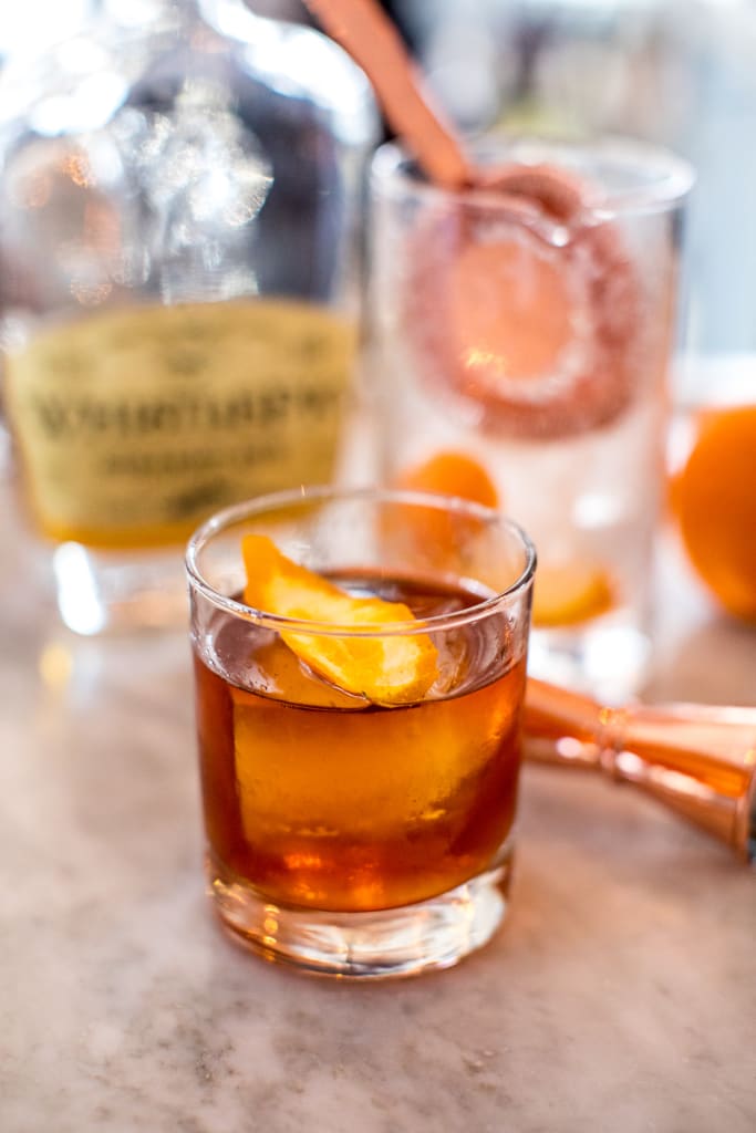 A glass of amber-colored whiskey with an orange peel garnish sits on a marble surface in Atlanta, Georgia.