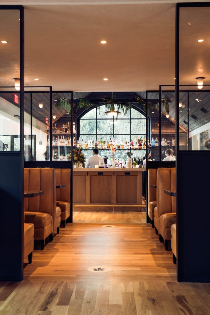 Modern restaurant interior with leather booths, wooden bar, and large window behind it in Atlanta, Georgia.