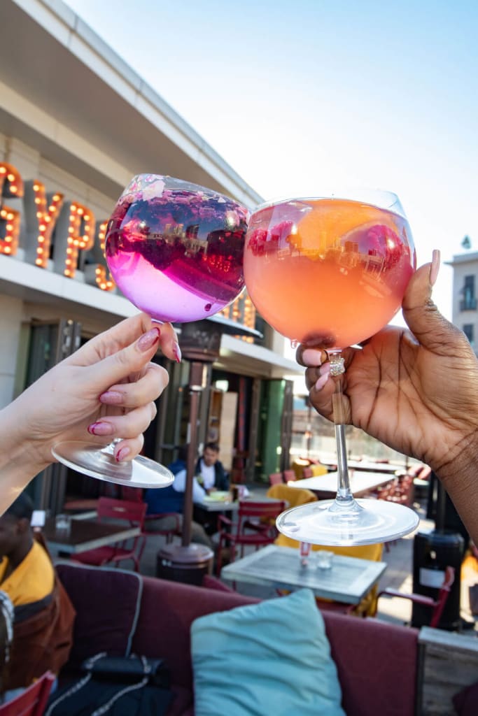 Two hands clink large, colorful cocktail glasses filled with fruity drinks outdoors in Atlanta, Georgia.