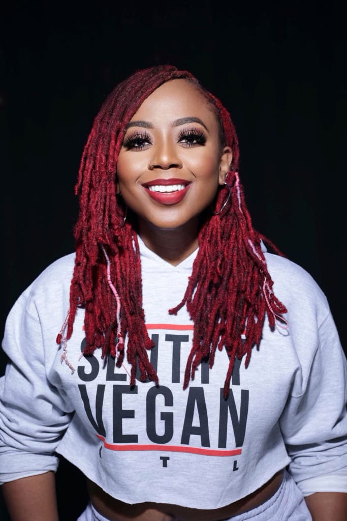 A smiling woman with vibrant red dreadlocks wears a cropped sweatshirt promoting veganism in Atlanta, Georgia.